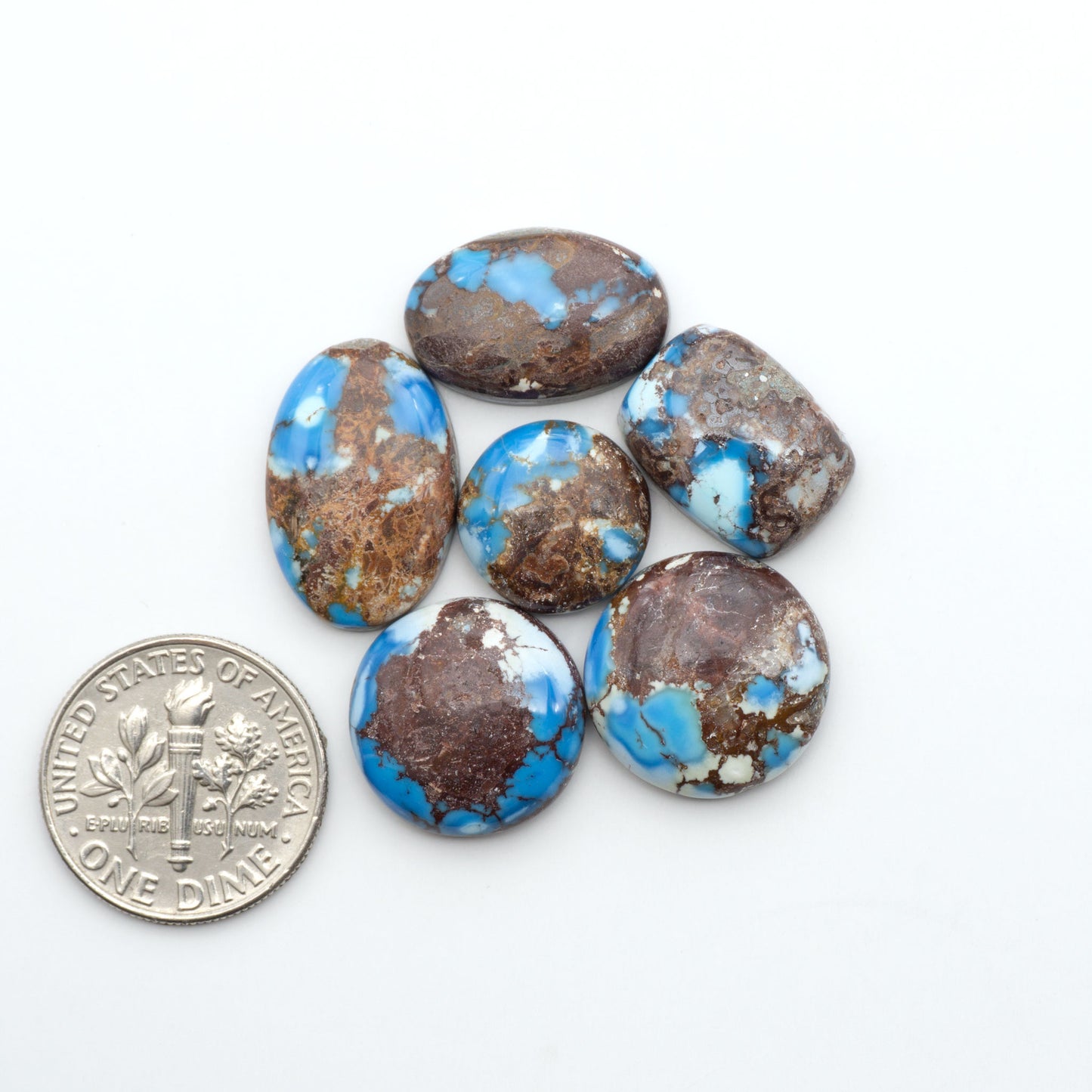 Golden Hills Turquoise cabochons, icy blue to lavender tones with chocolate matrix, polished stones on a white background with a US dime for scale