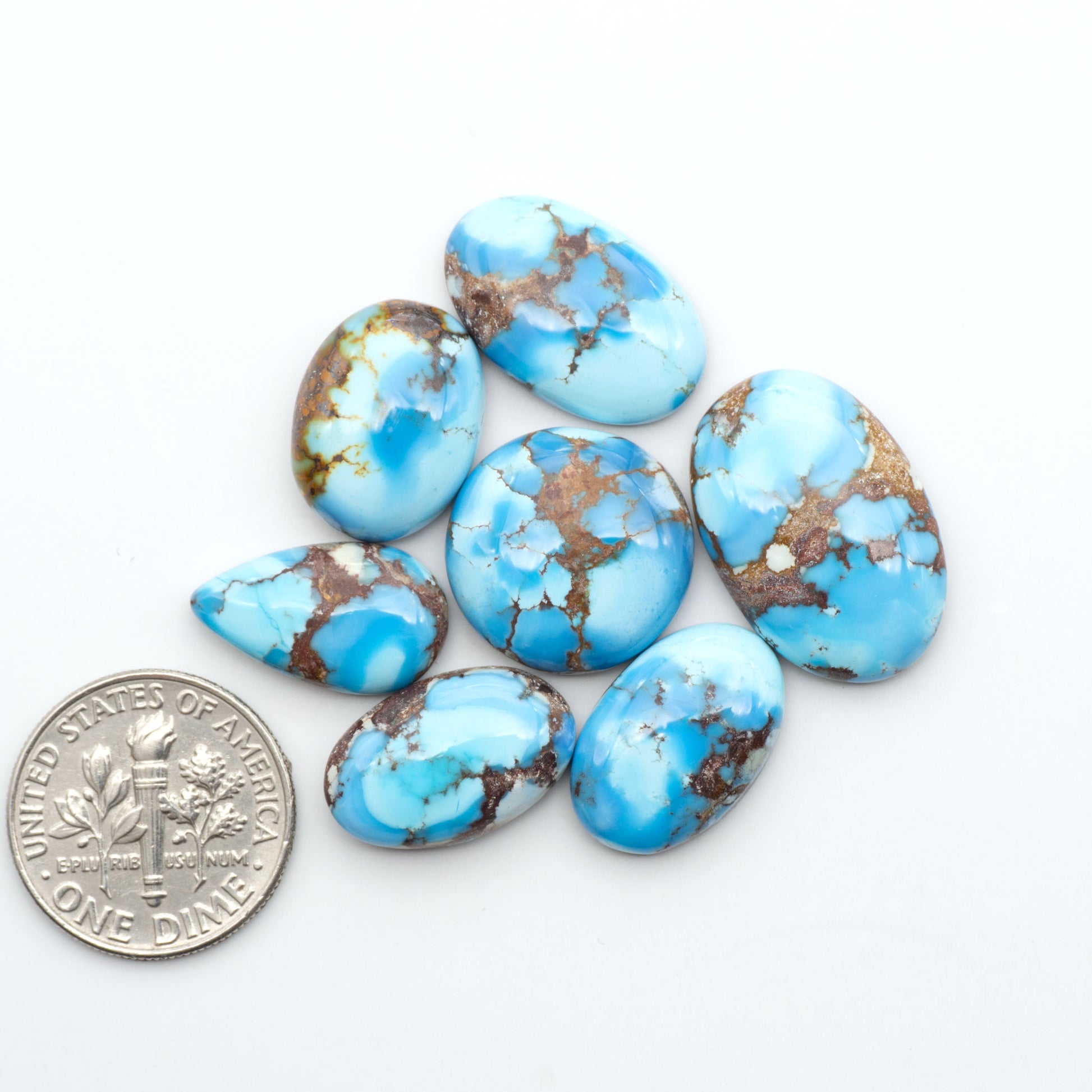 Golden Hills Turquoise cabochons, icy blue to lavender tones with chocolate matrix, polished stones on a white background with a US dime for scale