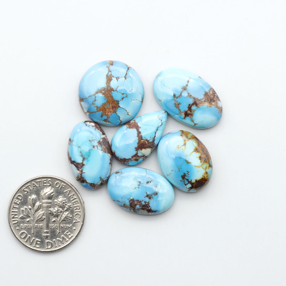 Golden Hills Turquoise cabochons, icy blue to lavender tones with chocolate matrix, polished stones on a white background with a US dime for scale