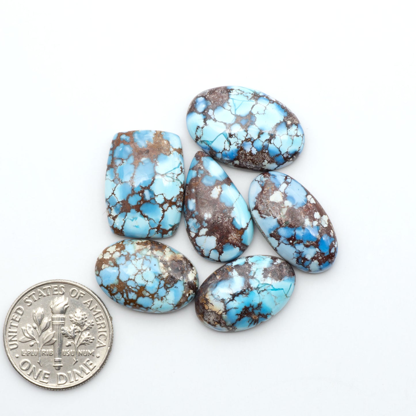 Golden Hills Turquoise cabochons, icy blue to lavender tones with chocolate matrix, polished stones on a white background with a US dime for scale