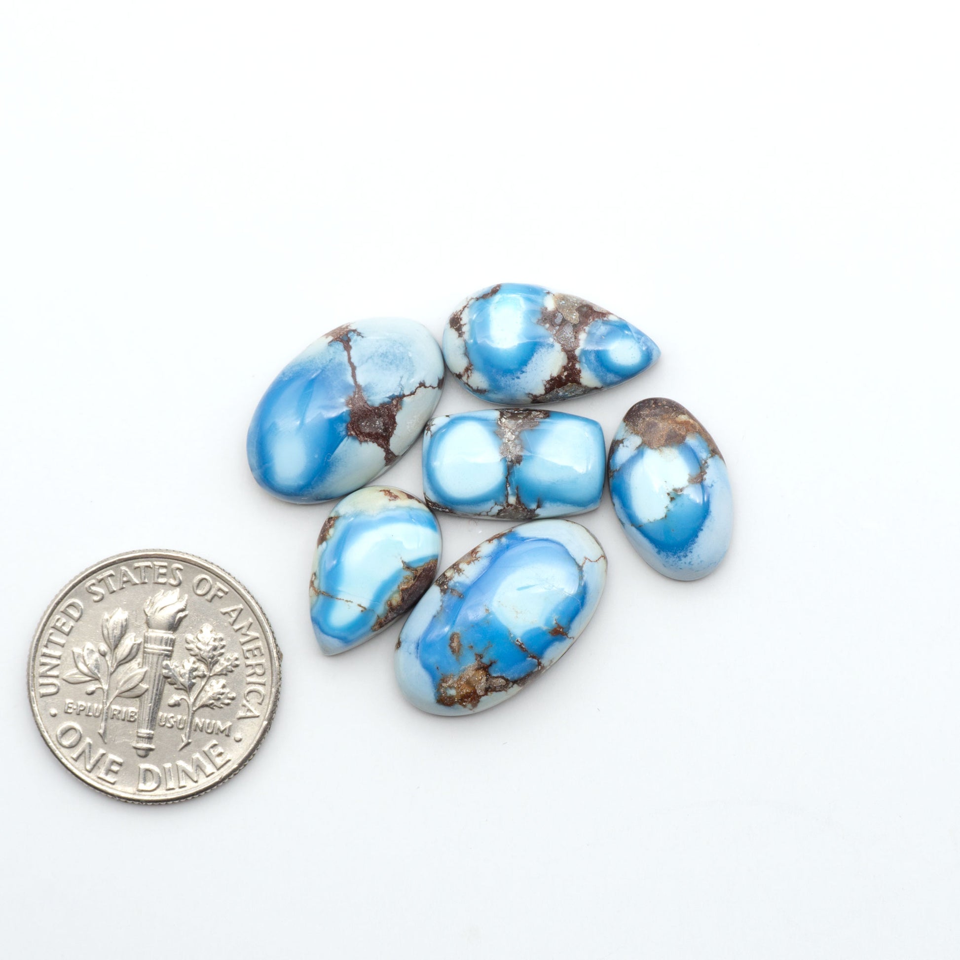 Golden Hills Turquoise cabochons, icy blue to lavender tones with chocolate matrix, polished stones on a white background with a US dime for scale
