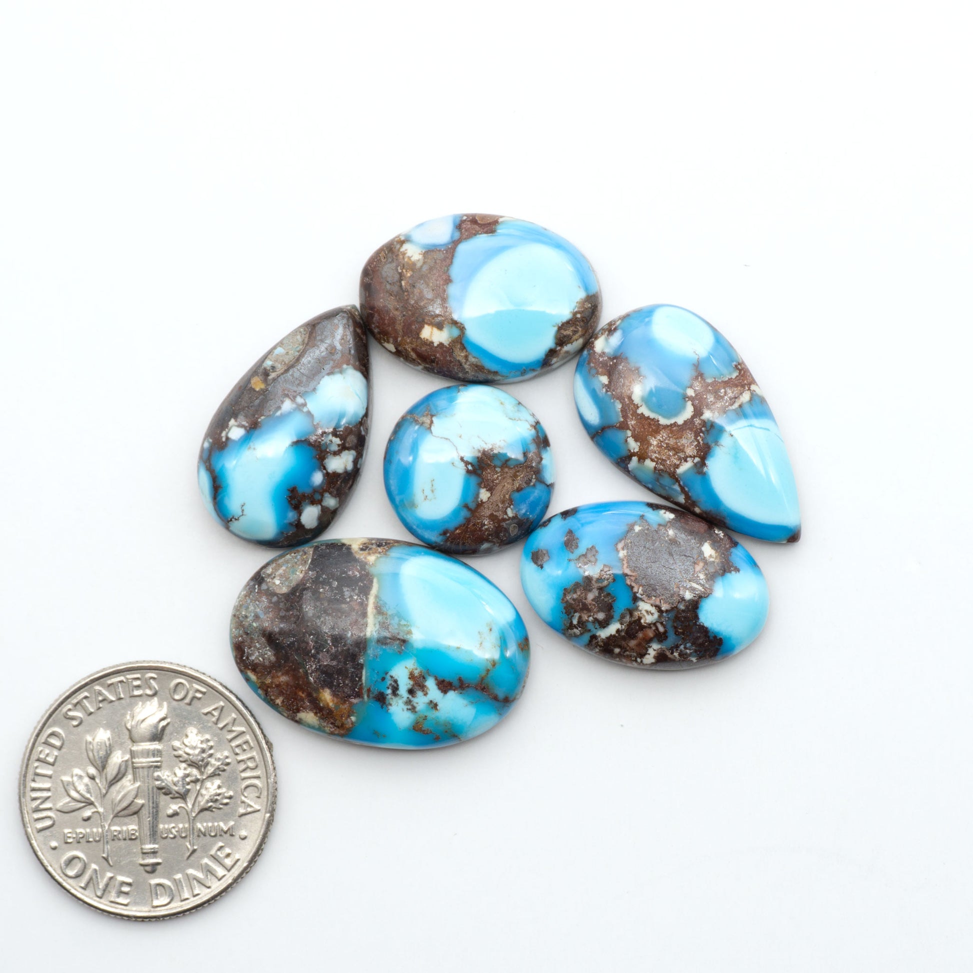 Golden Hills Turquoise cabochons, icy blue to lavender tones with chocolate matrix, polished stones on a white background with a US dime for scale