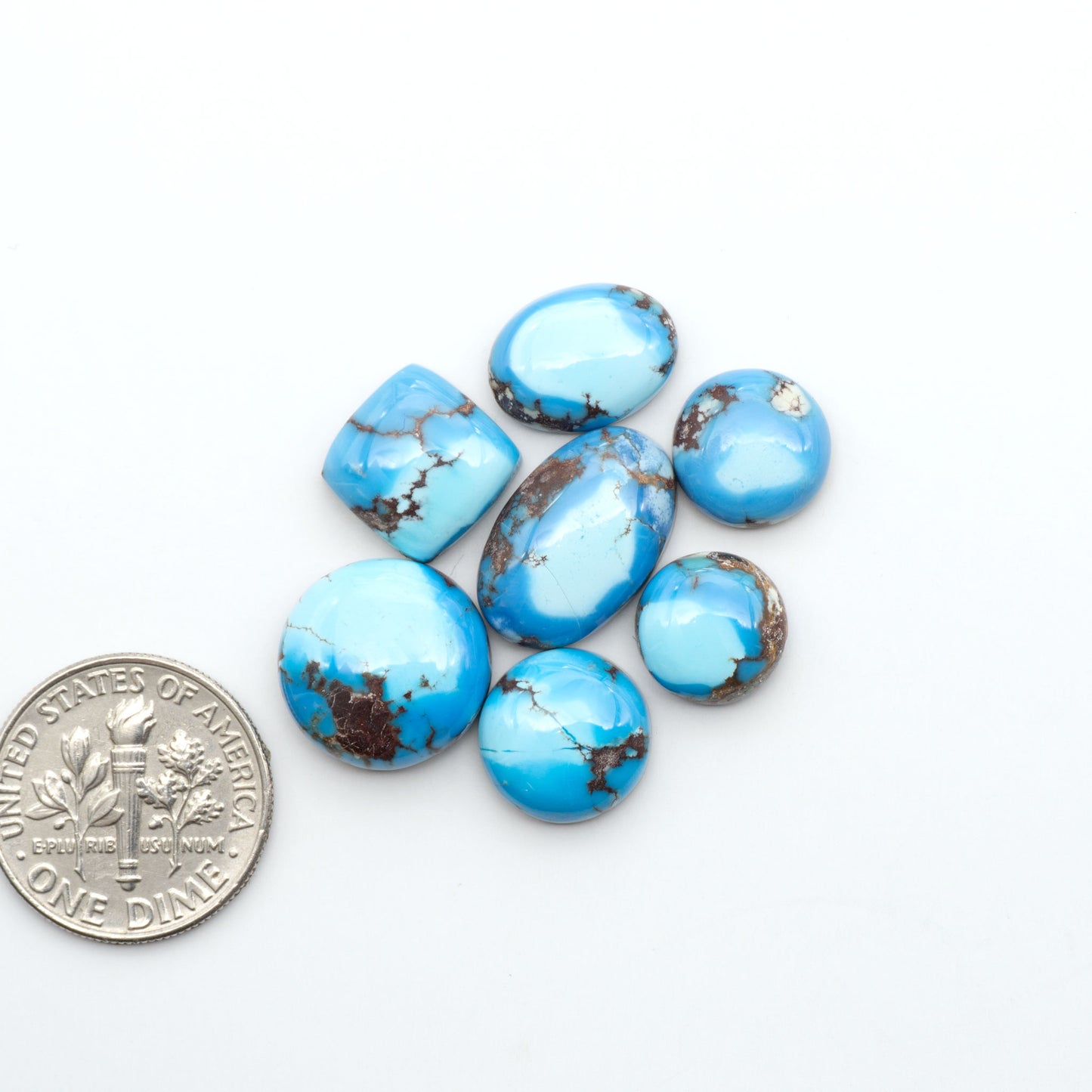 Golden Hills Turquoise cabochons, icy blue to lavender tones with chocolate matrix, polished stones on a white background with a US dime for scale