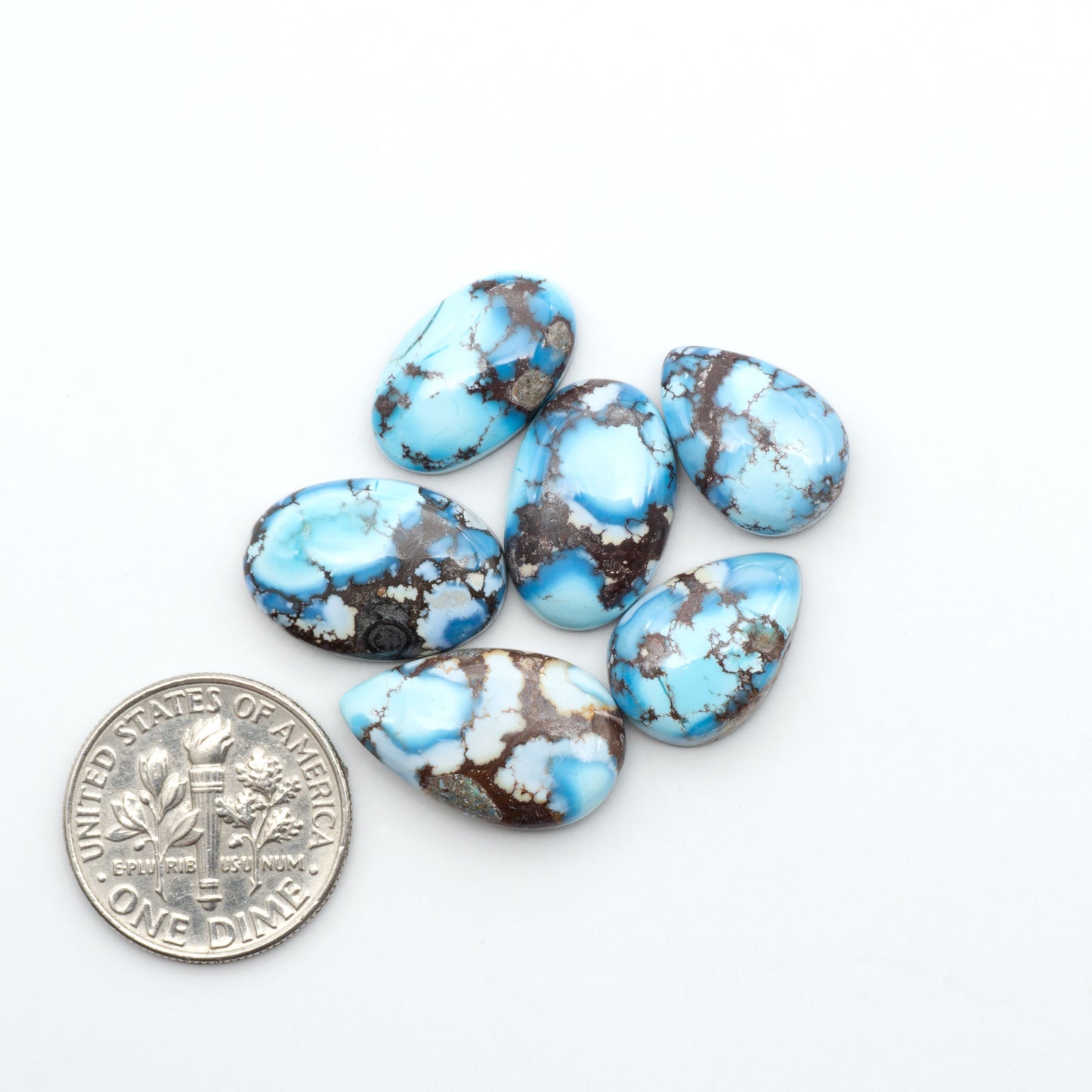 Golden Hills Turquoise cabochons, icy blue to lavender tones with chocolate matrix, polished stones on a white background with a US dime for scale
