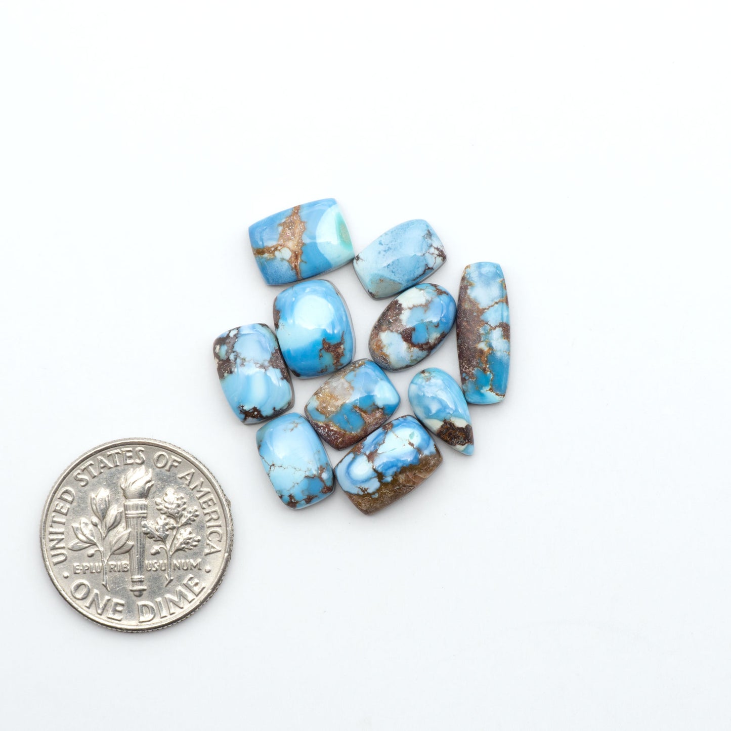 Golden Hills Turquoise cabochons, icy blue to lavender tones with chocolate matrix, polished stones on a white background with a US dime for scale