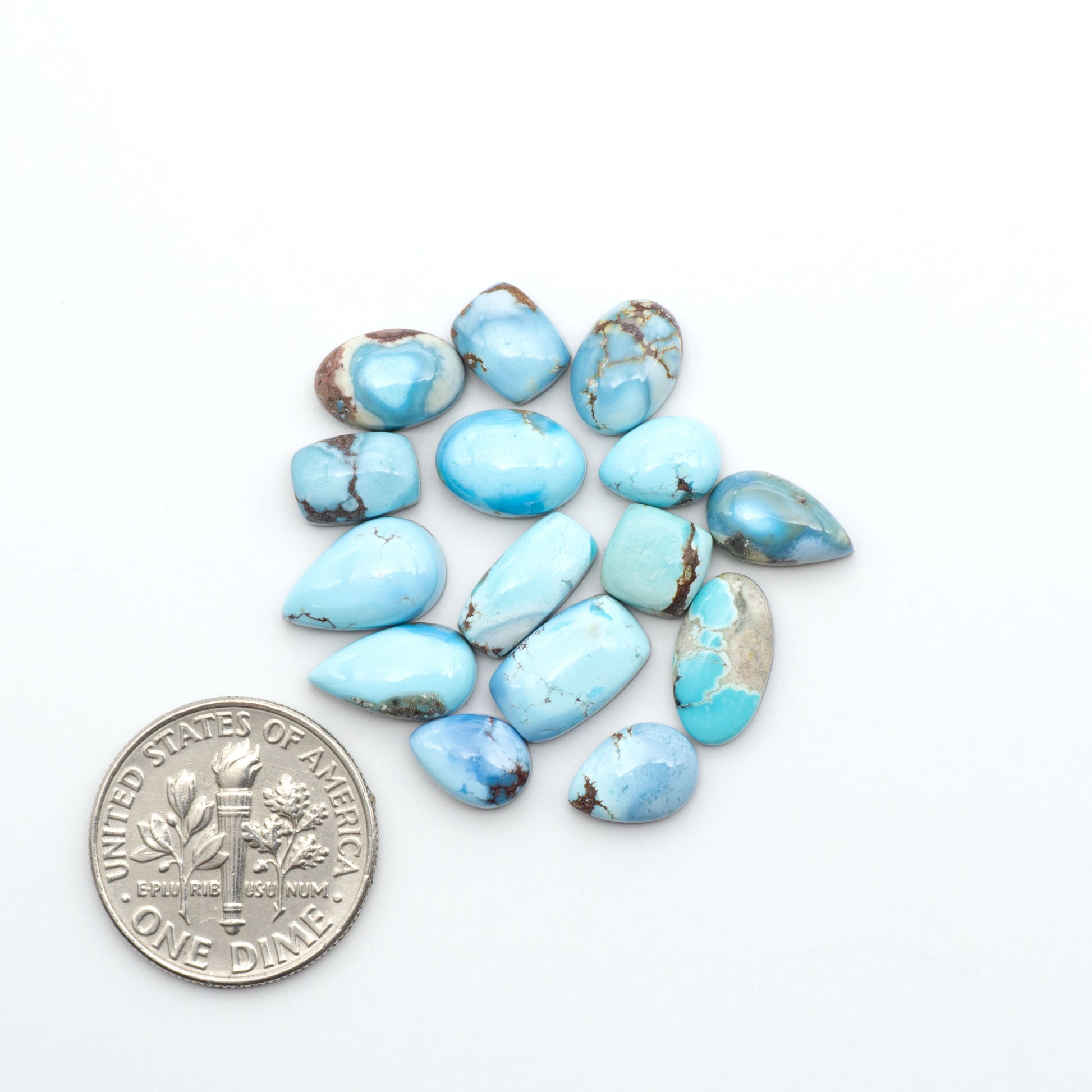 Golden Hills Turquoise cabochons, icy blue to lavender tones with chocolate matrix, polished stones on a white background with a US dime for scale