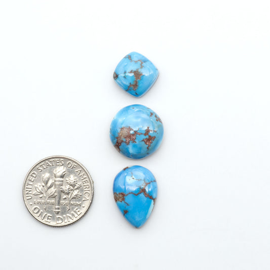 Golden Hills Turquoise cabochons, icy blue to lavender tones with chocolate matrix, polished stones on a white background with a US dime for scale