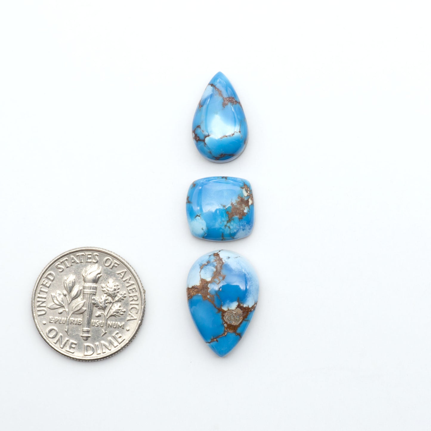Golden Hills Turquoise cabochons, icy blue to lavender tones with chocolate matrix, polished stones on a white background with a US dime for scale