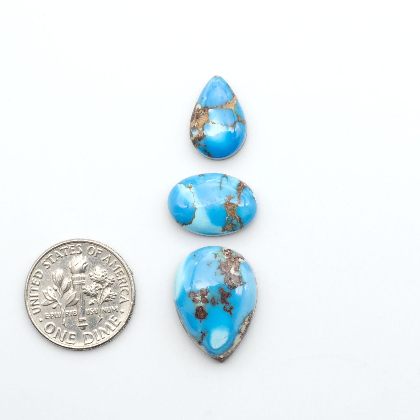 Golden Hills Turquoise cabochons, icy blue to lavender tones with chocolate matrix, polished stones on a white background with a US dime for scale