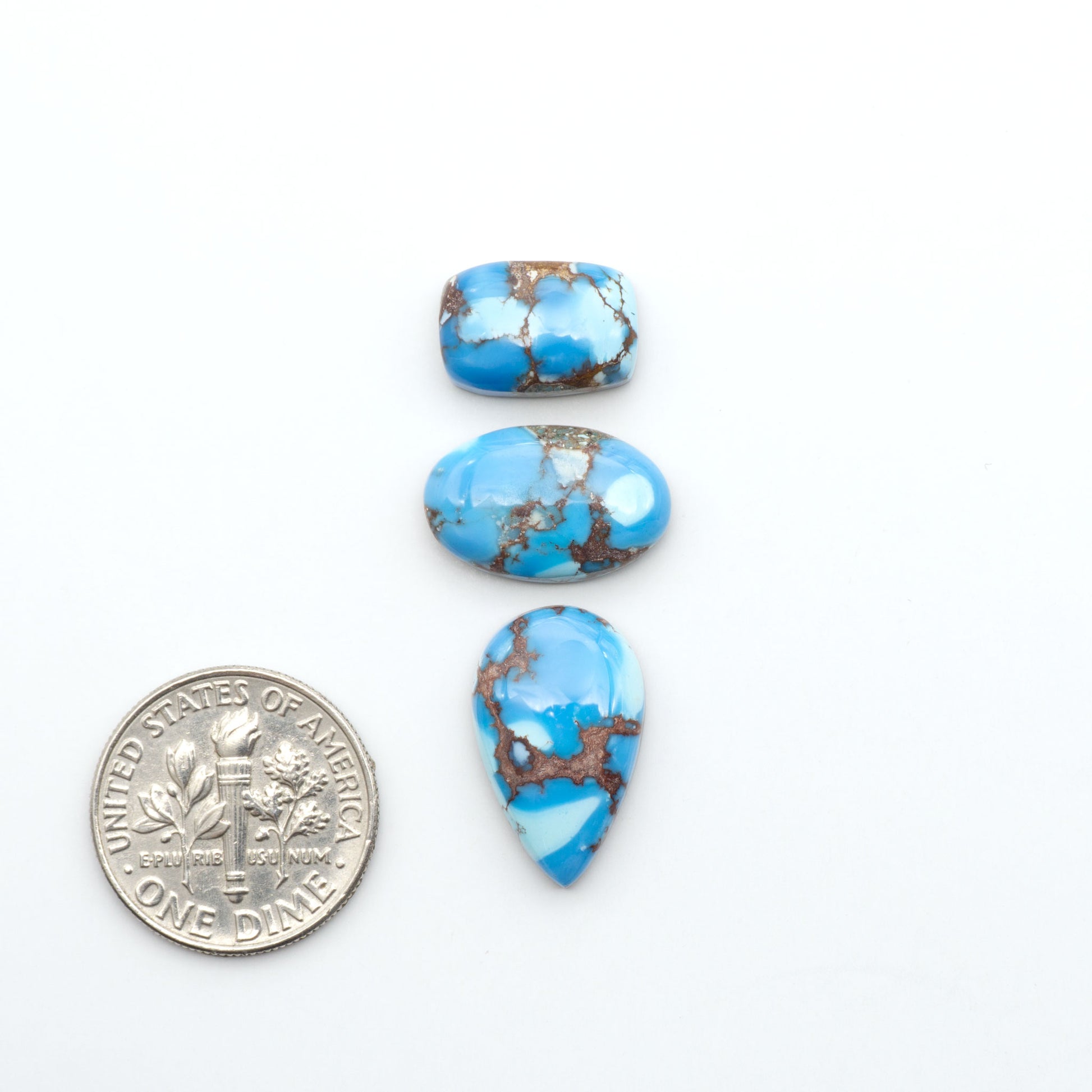 Golden Hills Turquoise cabochons, icy blue to lavender tones with chocolate matrix, polished stones on a white background with a US dime for scale
