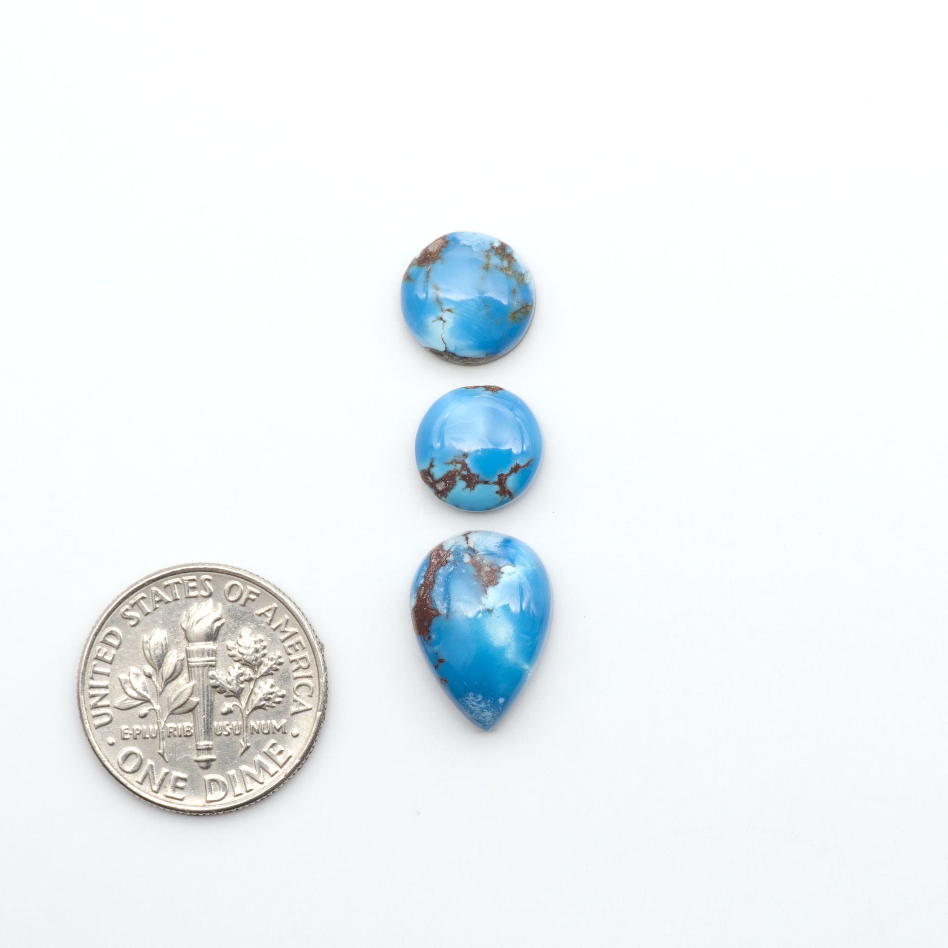 Golden Hills Turquoise cabochons, icy blue to lavender tones with chocolate matrix, polished stones on a white background with a US dime for scale