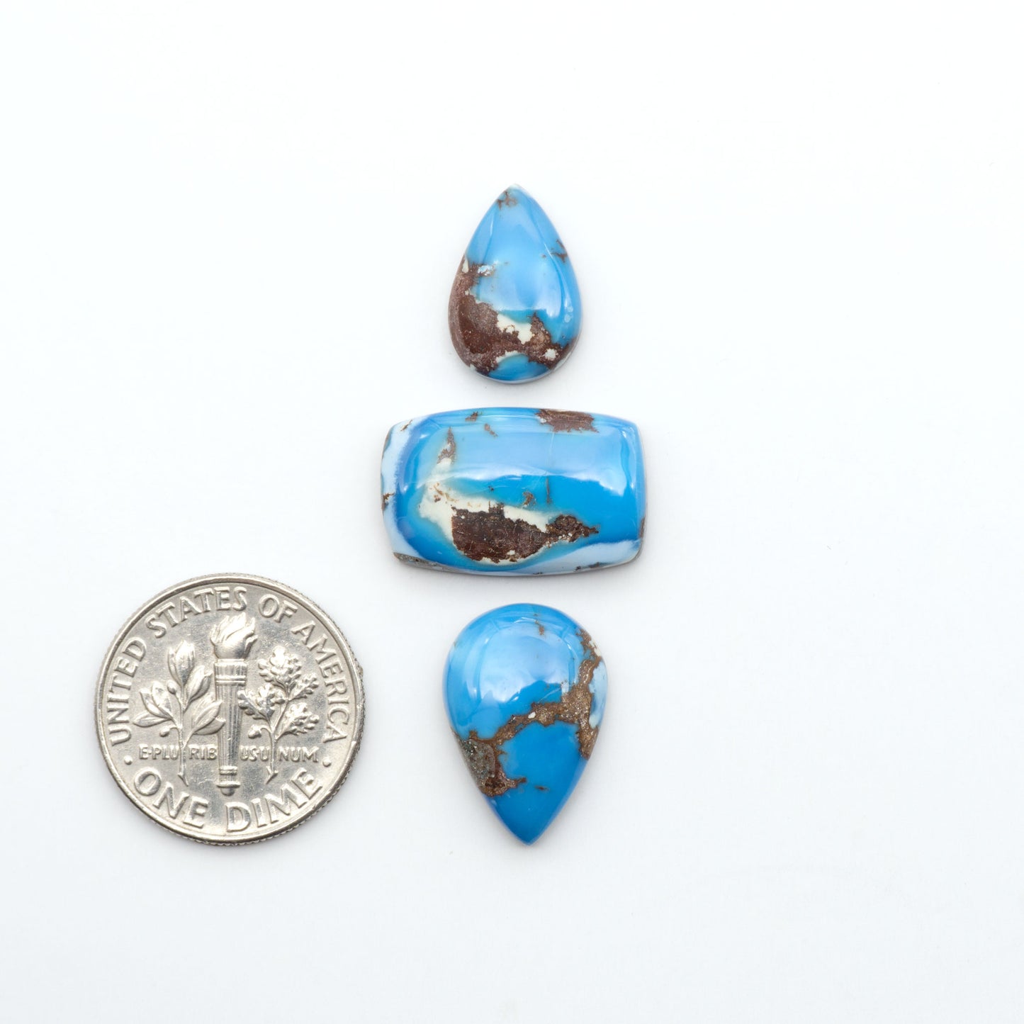 Golden Hills Turquoise cabochons, icy blue to lavender tones with chocolate matrix, polished stones on a white background with a US dime for scale