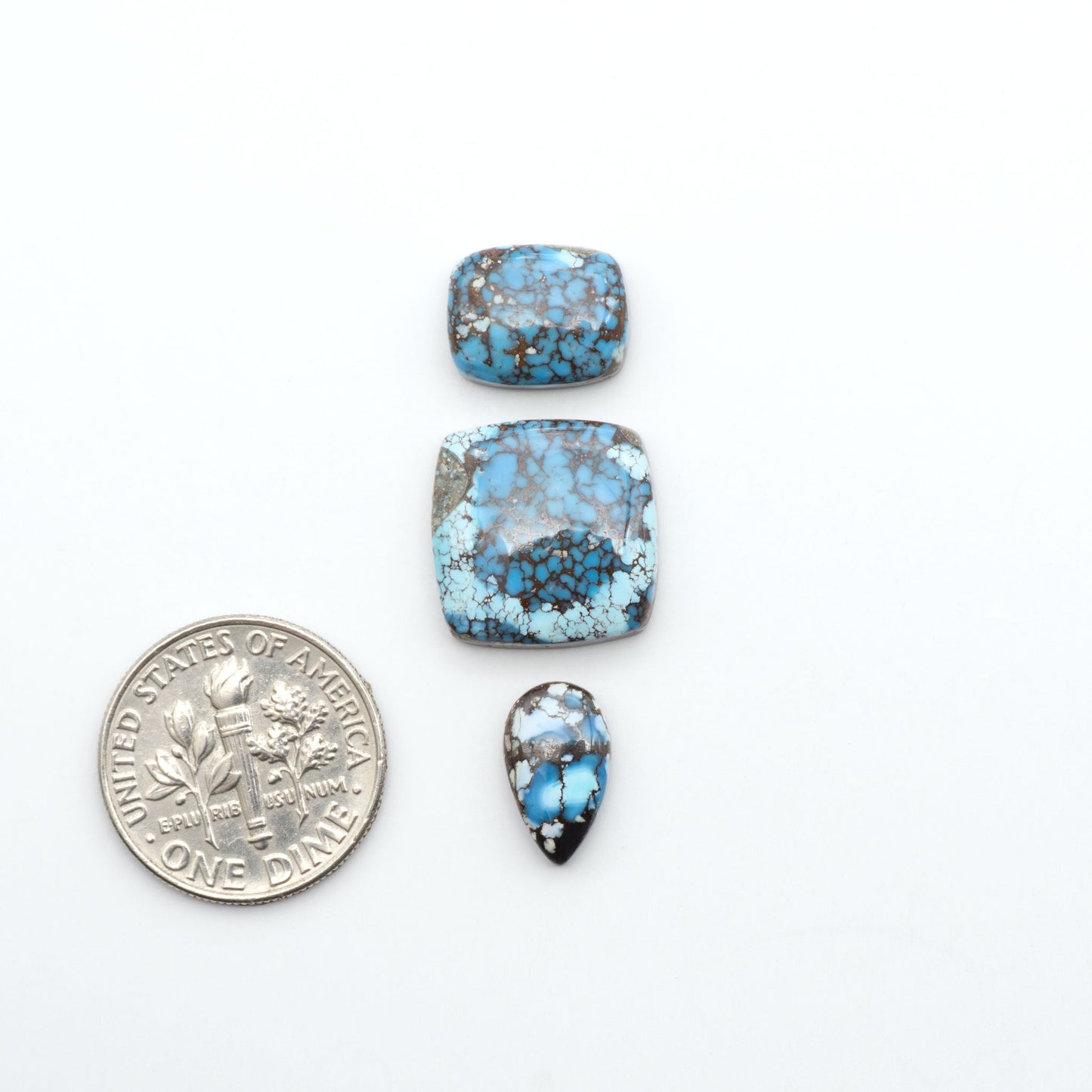 Golden Hills Turquoise cabochons, icy blue to lavender tones with chocolate matrix, polished stones on a white background with a US dime for scale