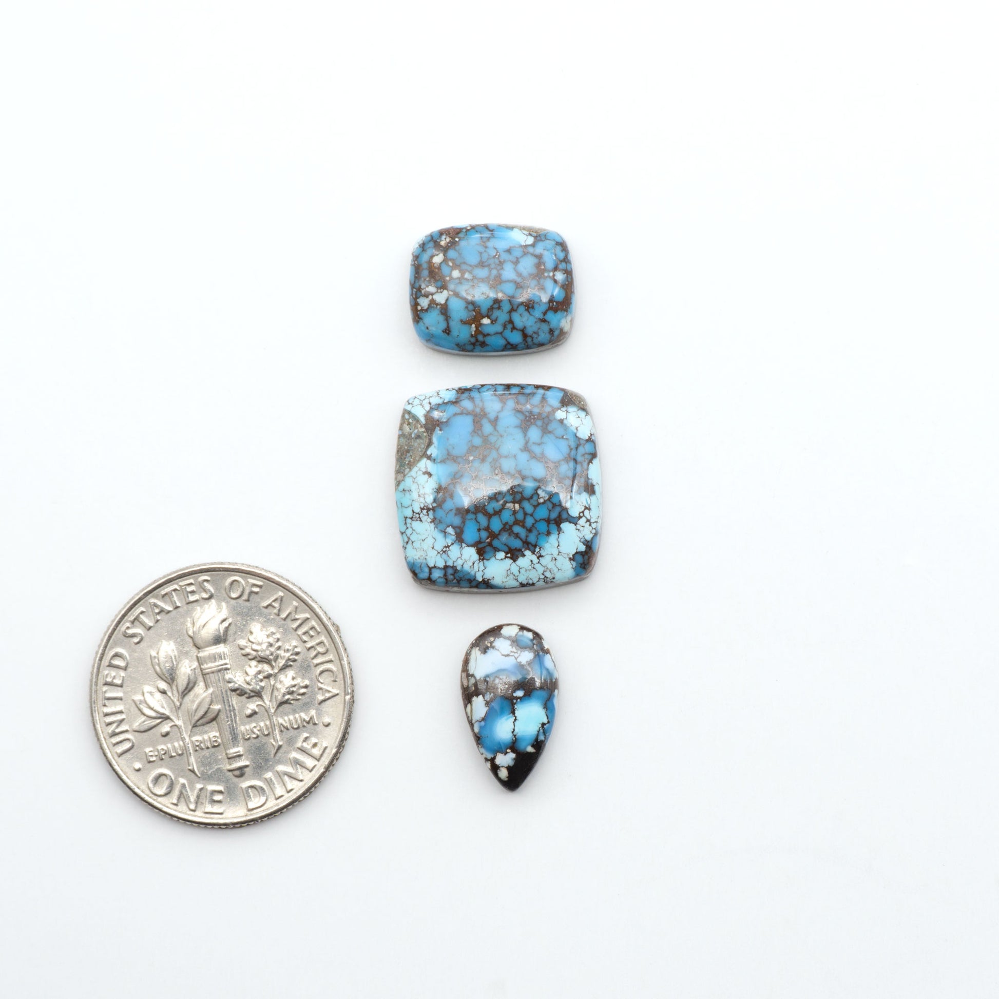 Golden Hills Turquoise cabochons, icy blue to lavender tones with chocolate matrix, polished stones on a white background with a US dime for scale