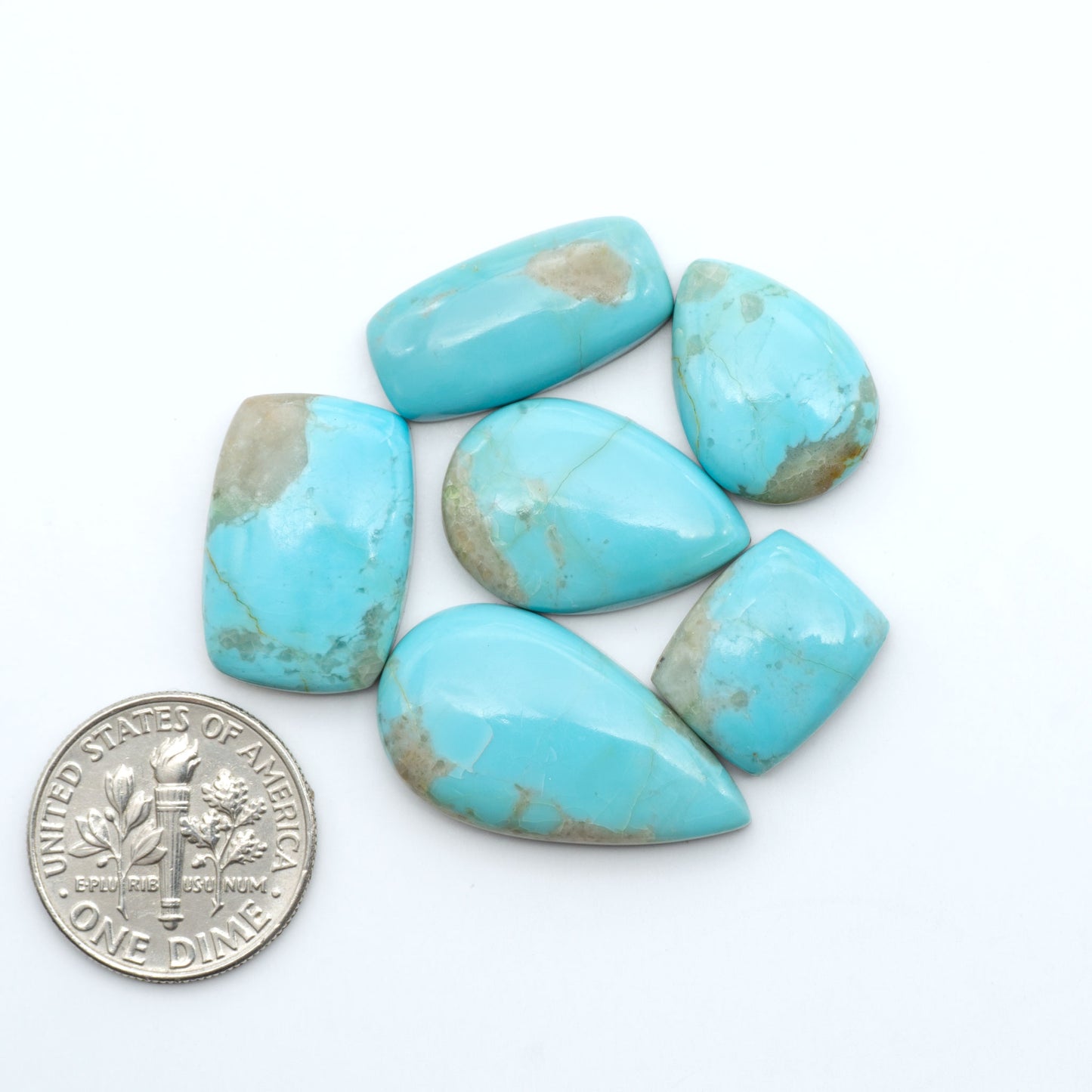 Pilot Mountain Turquoise cabochons, blue-green gemstones with natural matrix on a white background with a US dime for scale