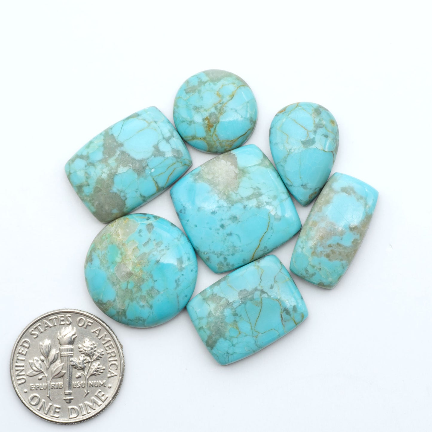 Pilot Mountain Turquoise cabochons, blue-green gemstones with natural matrix on a white background with a US dime for scale