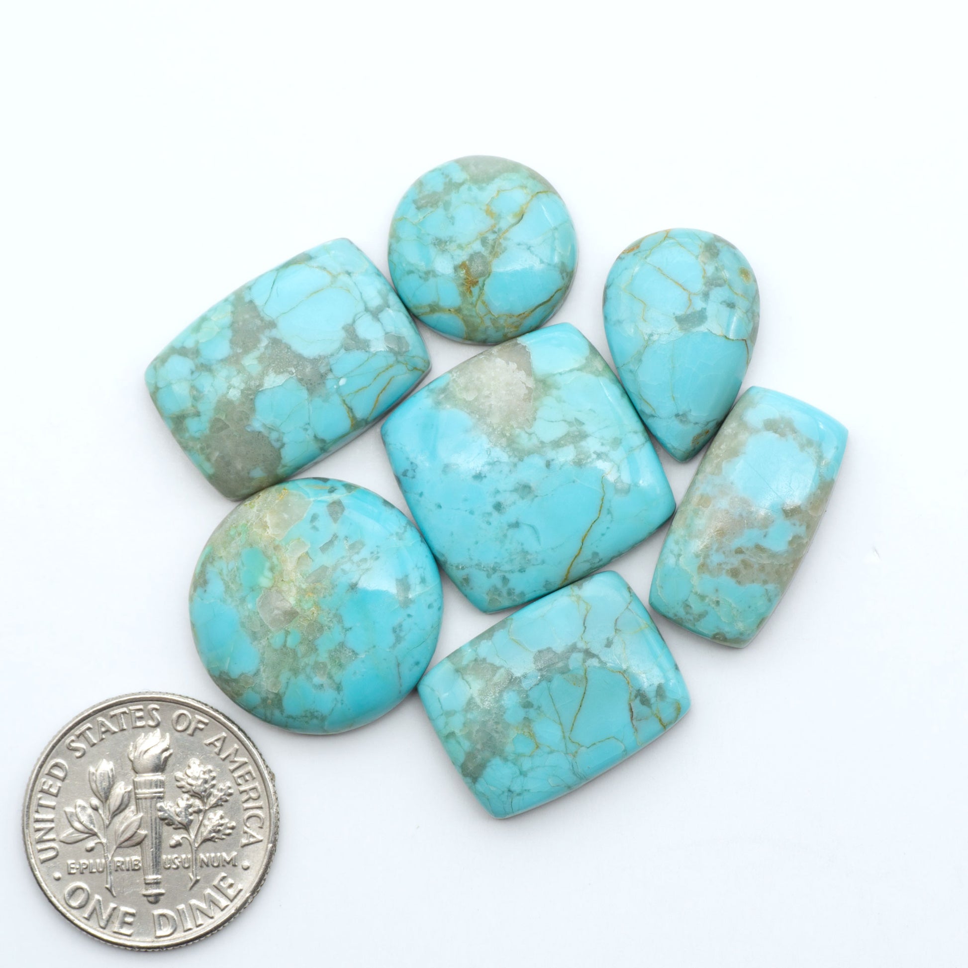 Pilot Mountain Turquoise cabochons, blue-green gemstones with natural matrix on a white background with a US dime for scale