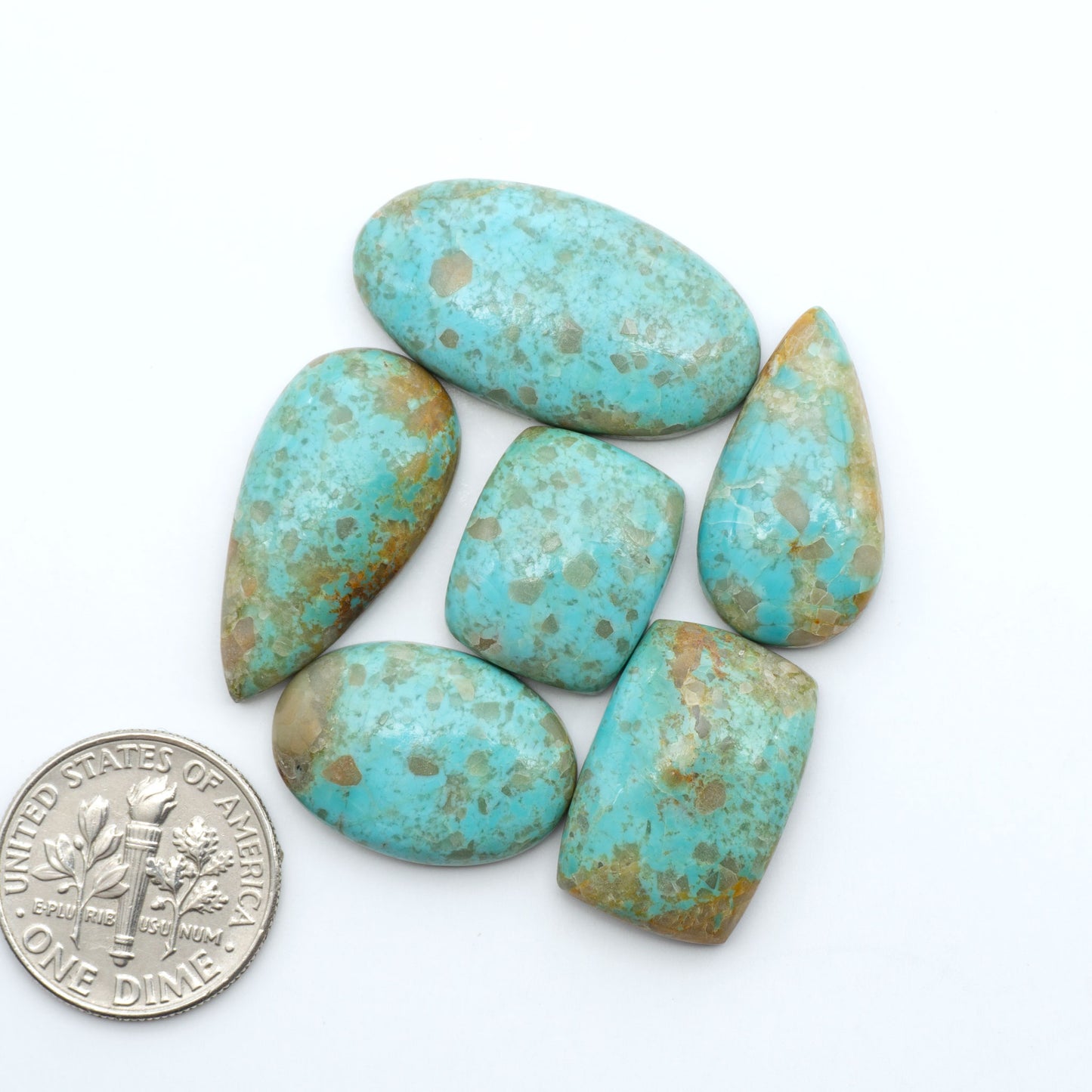Pilot Mountain Turquoise cabochons, blue-green gemstones with natural matrix on a white background with a US dime for scale