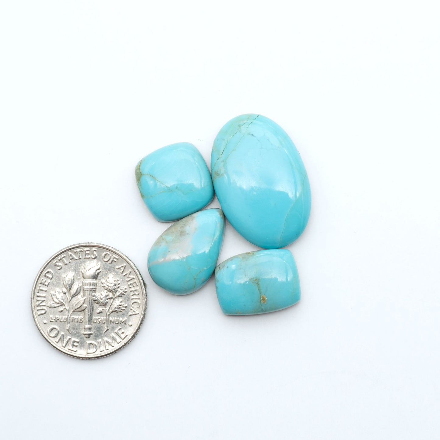 Pilot Mountain Turquoise cabochons, blue-green gemstones with natural matrix on a white background with a US dime for scale