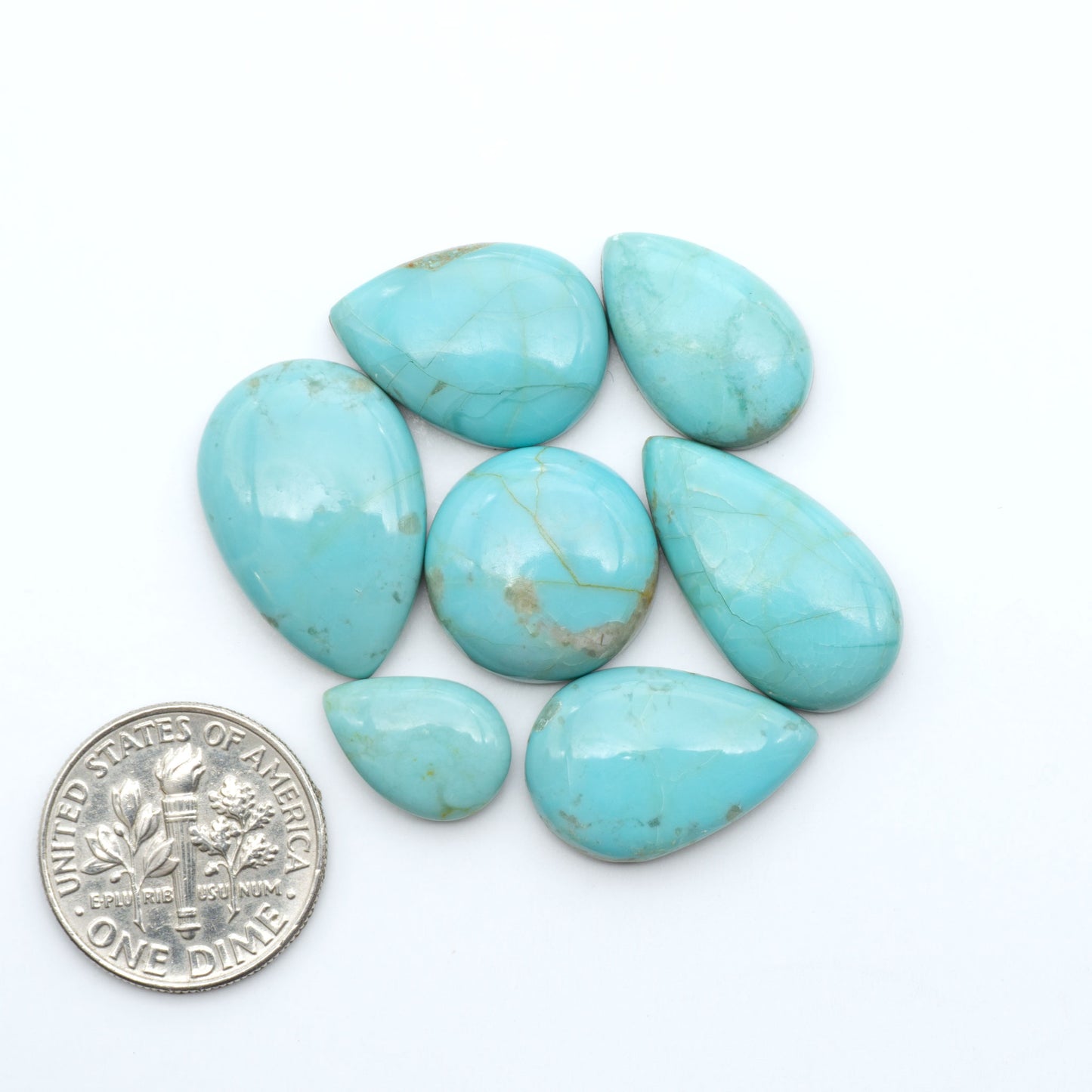Pilot Mountain Turquoise cabochons, blue-green gemstones with natural matrix on a white background with a US dime for scale