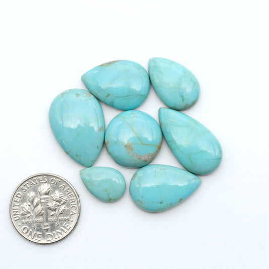 Pilot Mountain Turquoise cabochons, blue-green gemstones with natural matrix on a white background with a US dime for scale