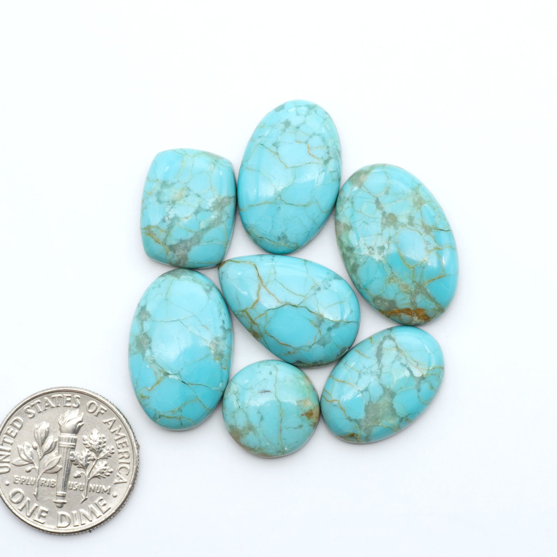 Pilot Mountain Turquoise cabochons, blue-green gemstones with natural matrix on a white background with a US dime for scale