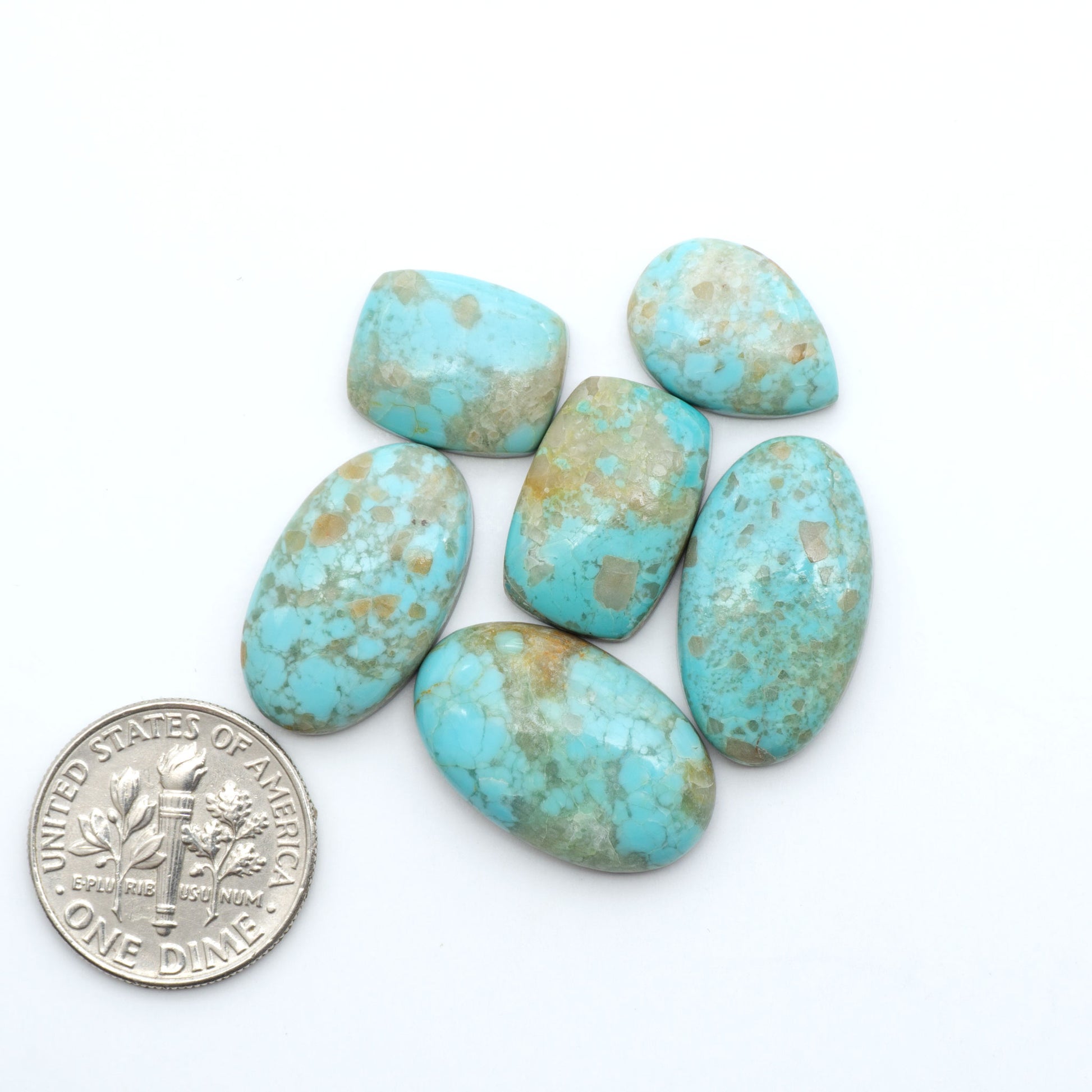Pilot Mountain Turquoise cabochons, blue-green gemstones with natural matrix on a white background with a US dime for scale