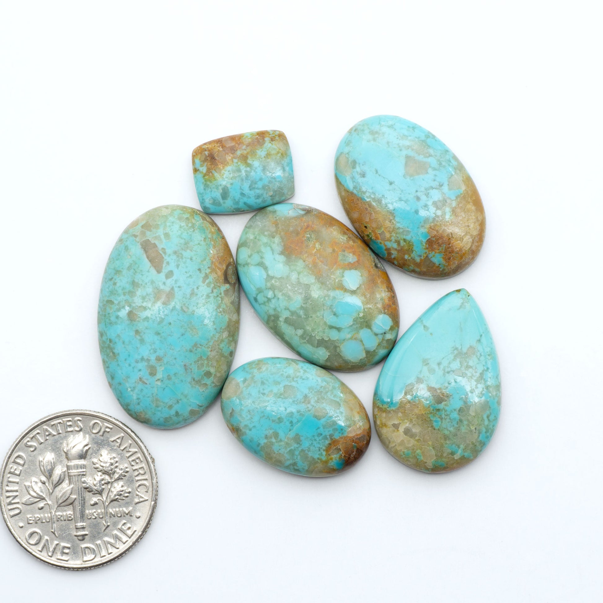 Pilot Mountain Turquoise cabochons, blue-green gemstones with natural matrix on a white background with a US dime for scale
