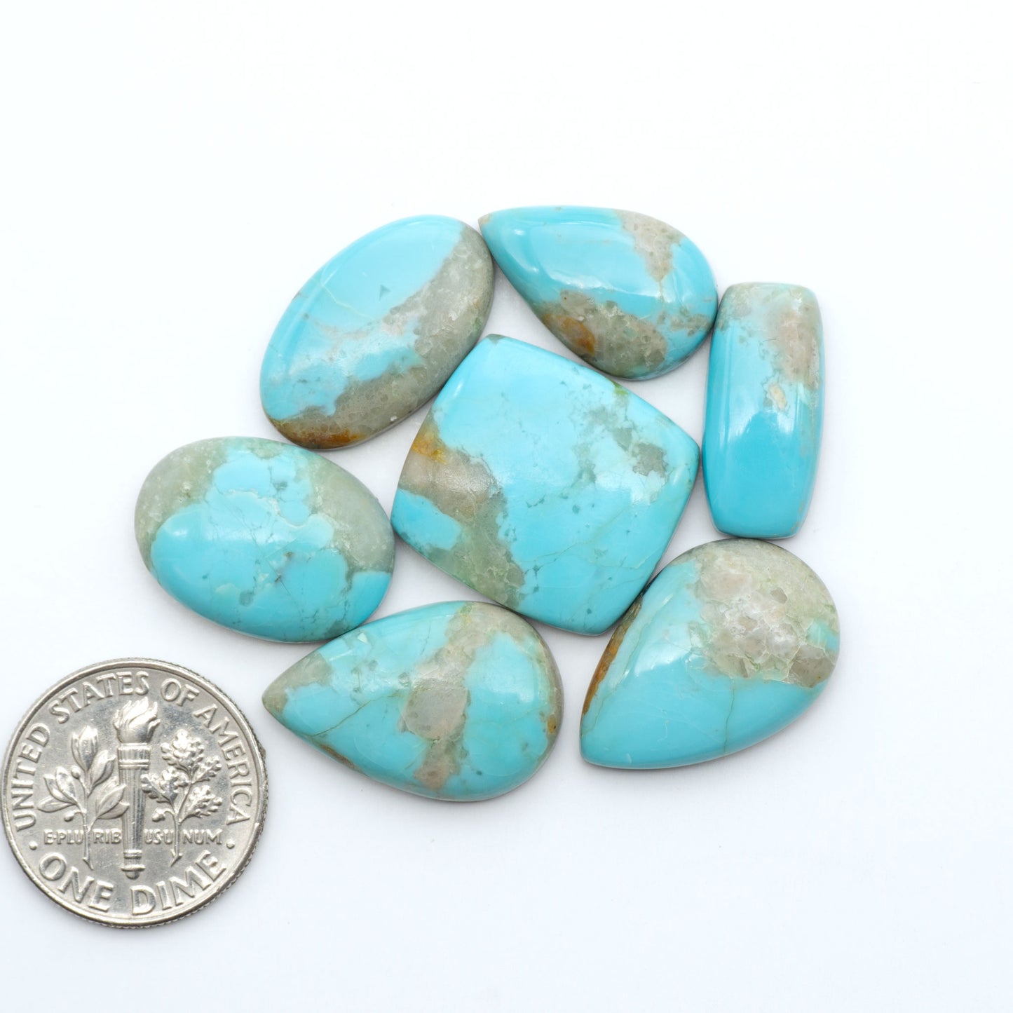 Pilot Mountain Turquoise cabochons, blue-green gemstones with natural matrix on a white background with a US dime for scale