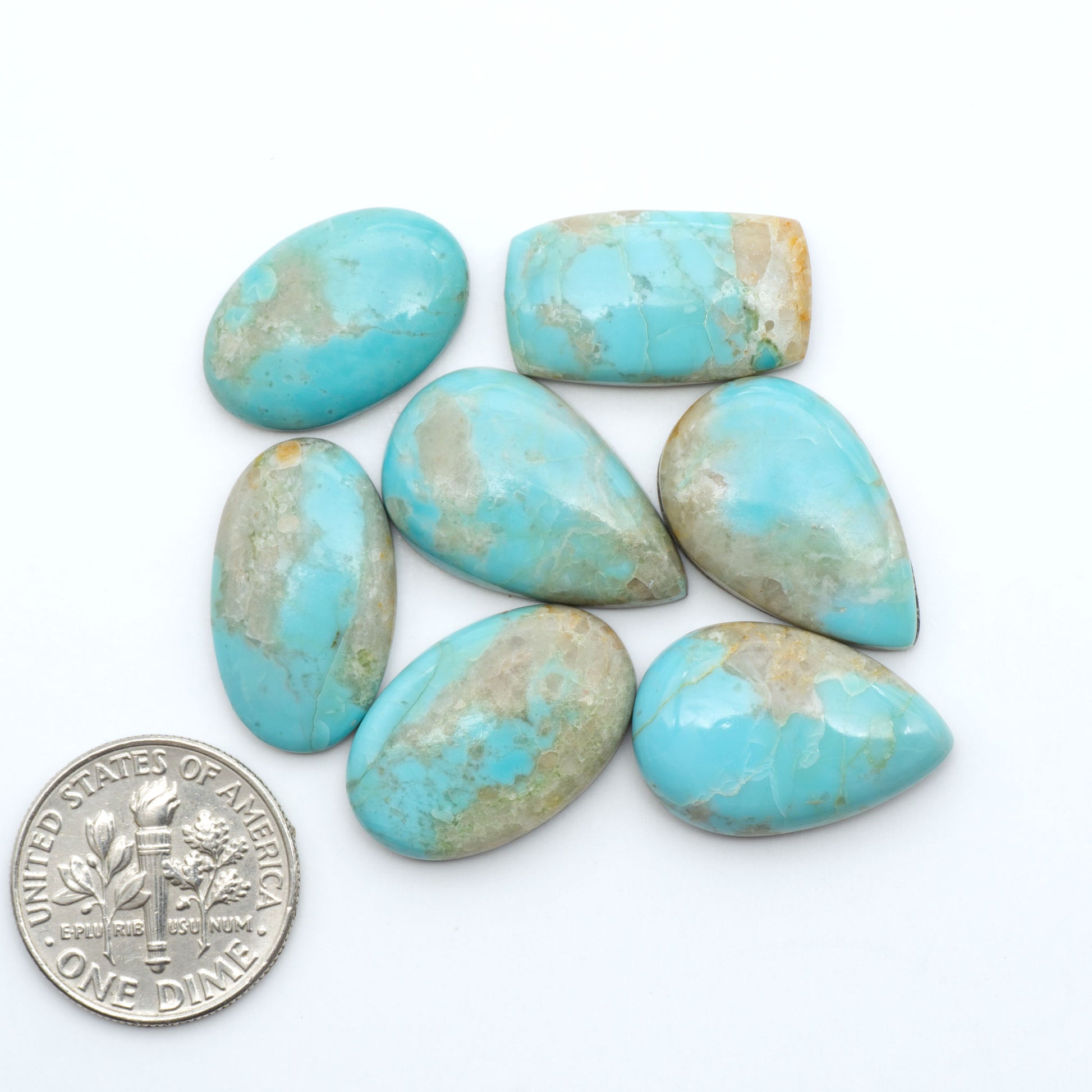 Pilot Mountain Turquoise cabochons, blue-green gemstones with natural matrix on a white background with a US dime for scale