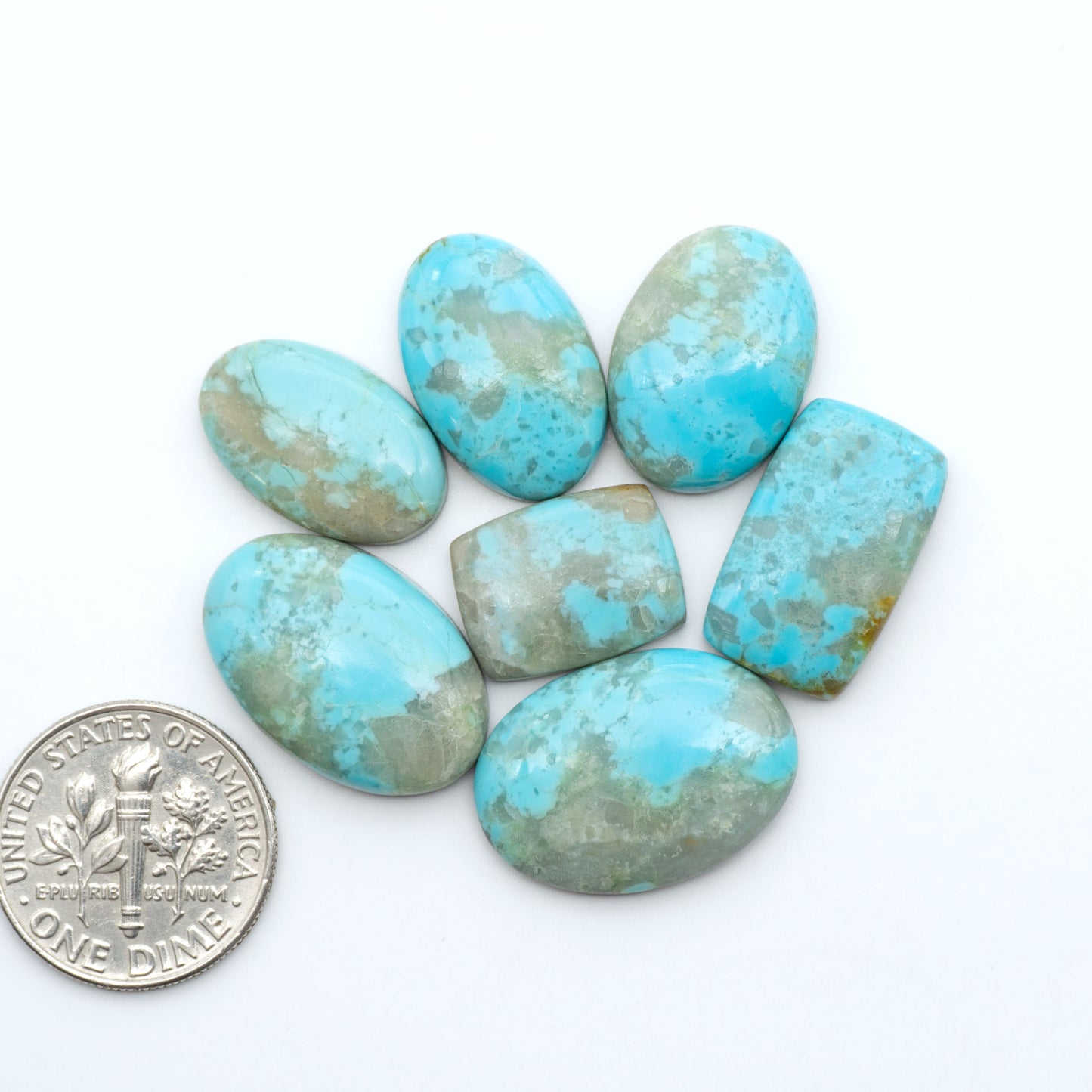 Pilot Mountain Turquoise cabochons, blue-green gemstones with natural matrix on a white background with a US dime for scale