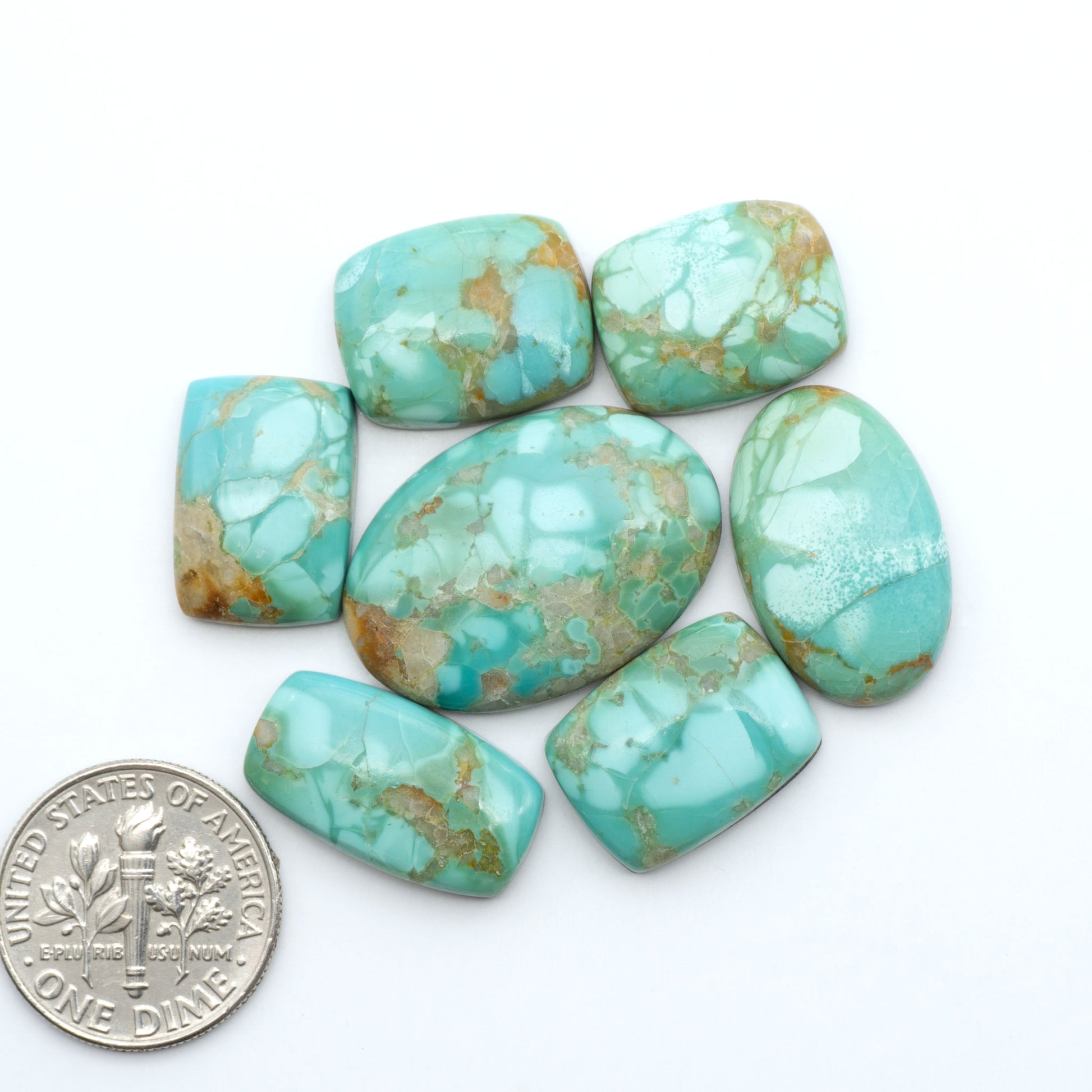 Pilot Mountain Turquoise cabochons, blue-green gemstones with natural matrix on a white background with a US dime for scale