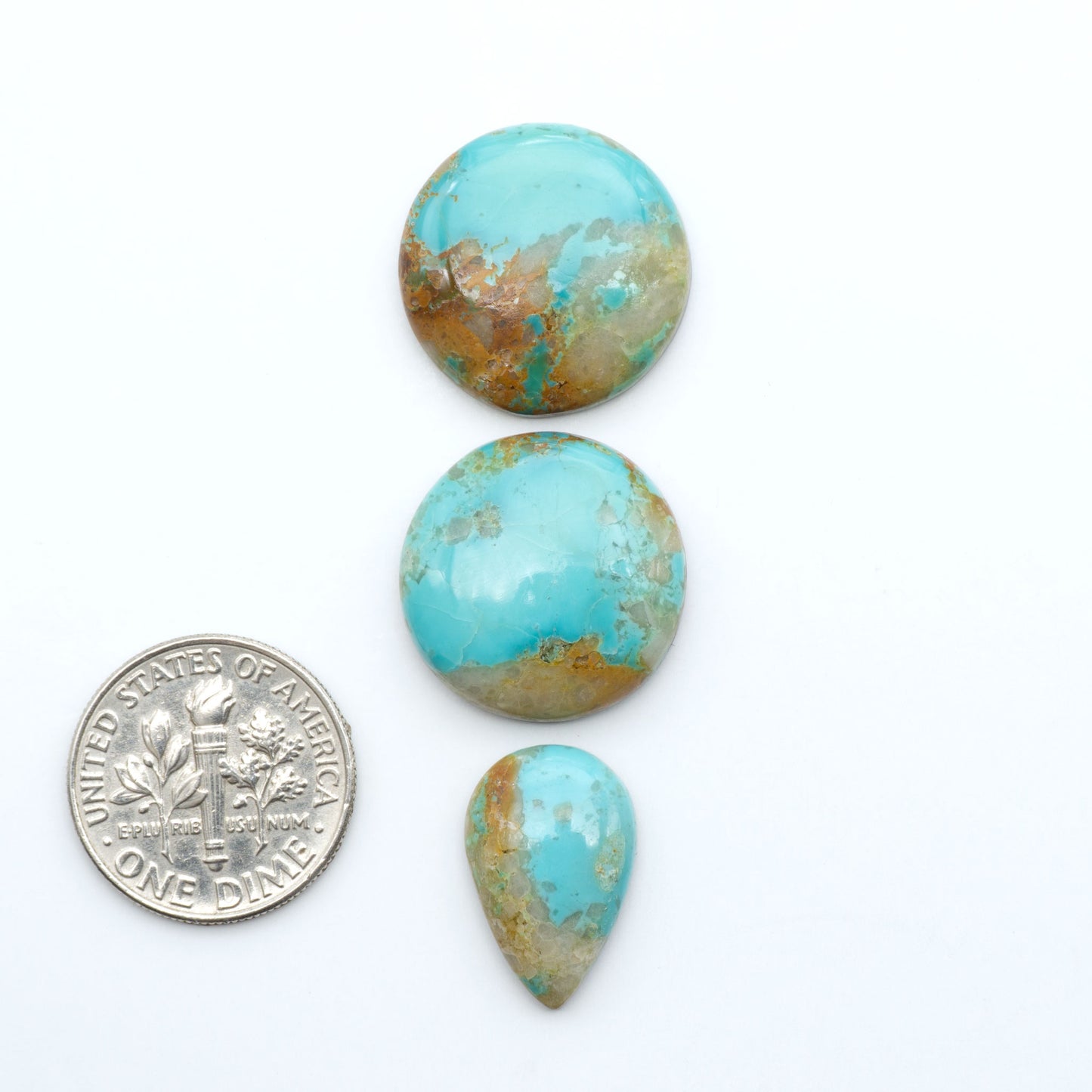 Pilot Mountain Turquoise cabochons, blue-green gemstones with natural matrix on a white background with a US dime for scale