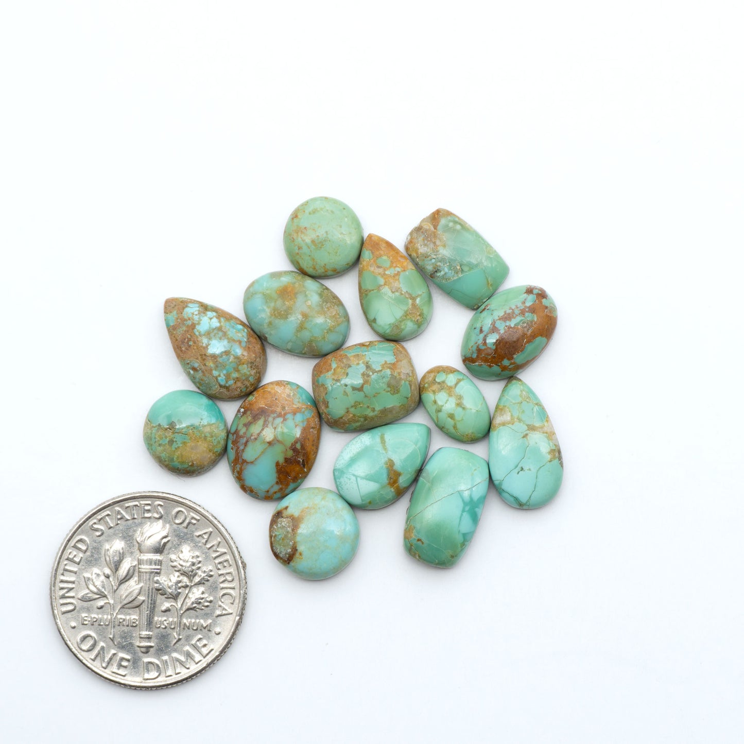 Pilot Mountain Turquoise cabochons, blue-green gemstones with natural matrix on a white background with a US dime for scale