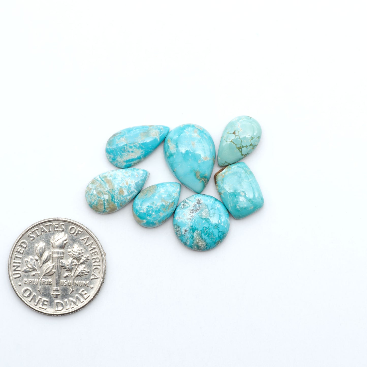 Fox Turquoise cabochons, polished gemstones with natural matrix on a white background, with a US dime for scale