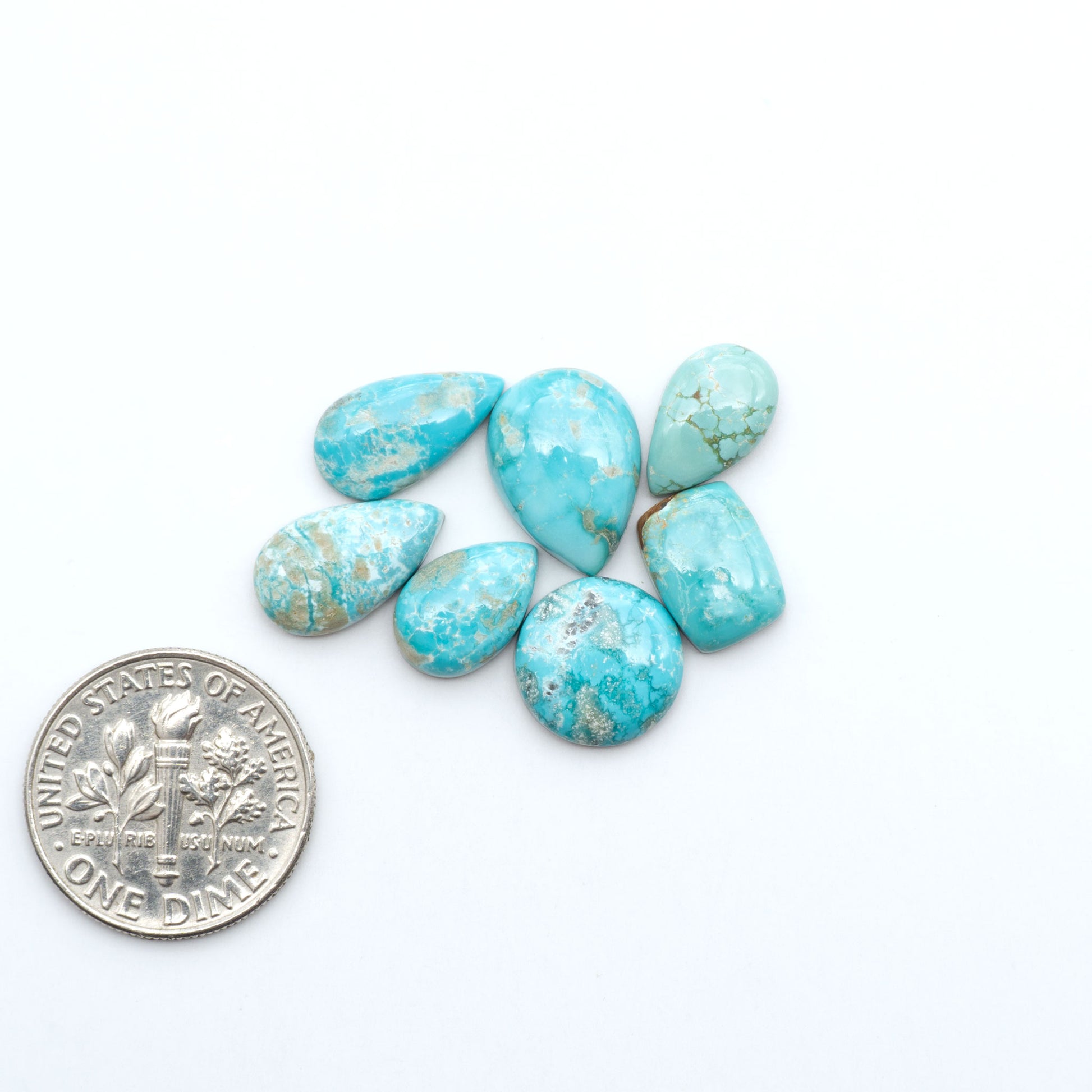 Fox Turquoise cabochons, polished gemstones with natural matrix on a white background, with a US dime for scale