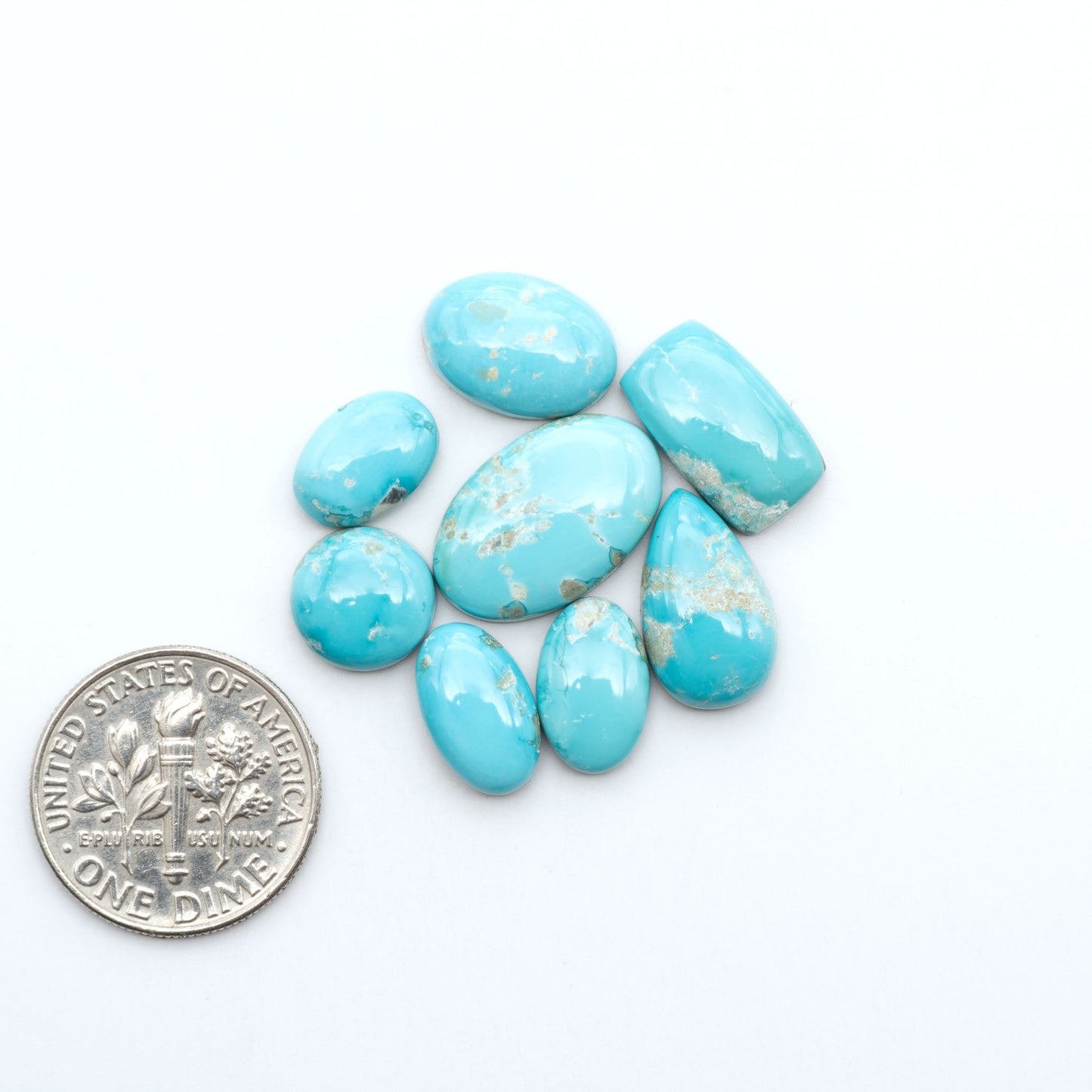 Fox Turquoise cabochons, polished gemstones with natural matrix on a white background, with a US dime for scale