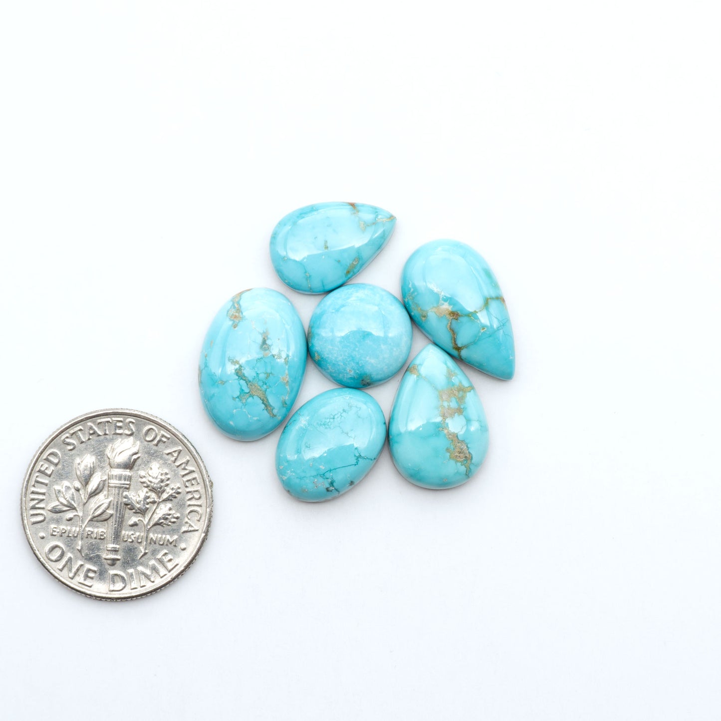Fox Turquoise cabochons, polished gemstones with natural matrix on a white background, with a US dime for scale