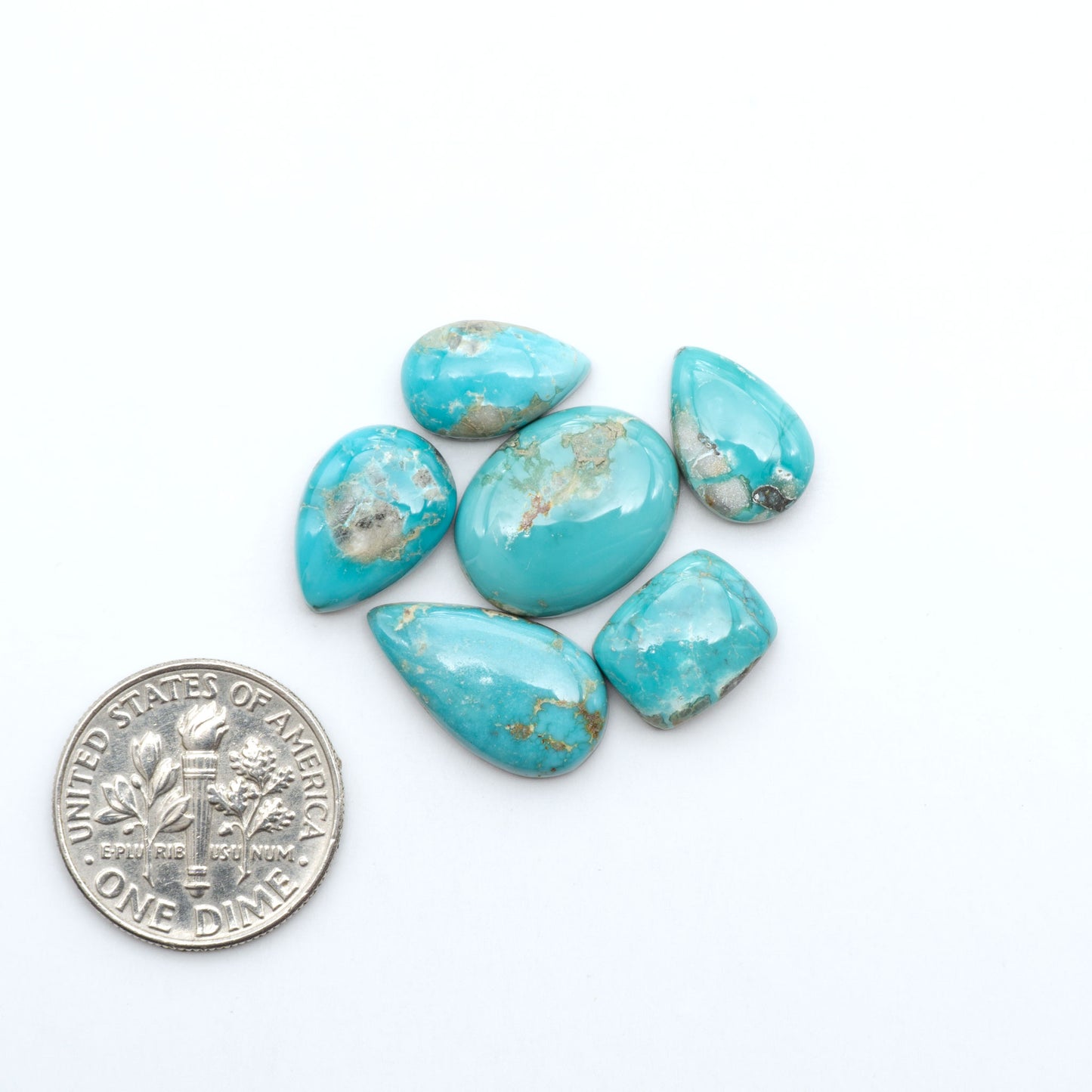 Fox Turquoise cabochons, polished gemstones with natural matrix on a white background, with a US dime for scale