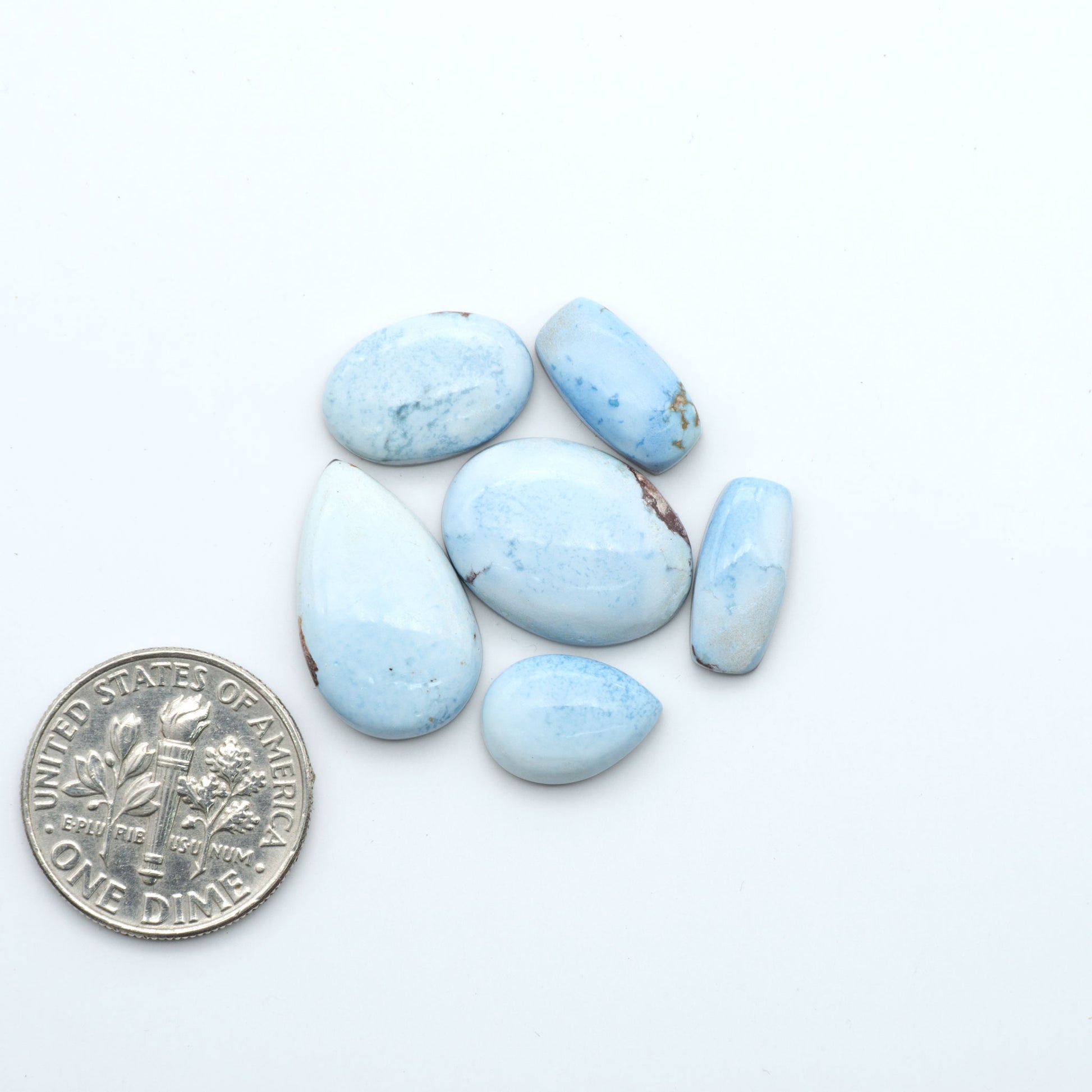 Golden Hills Turquoise cabochons, icy blue to lavender tones with chocolate matrix, polished stones on a white background with a US dime for scale