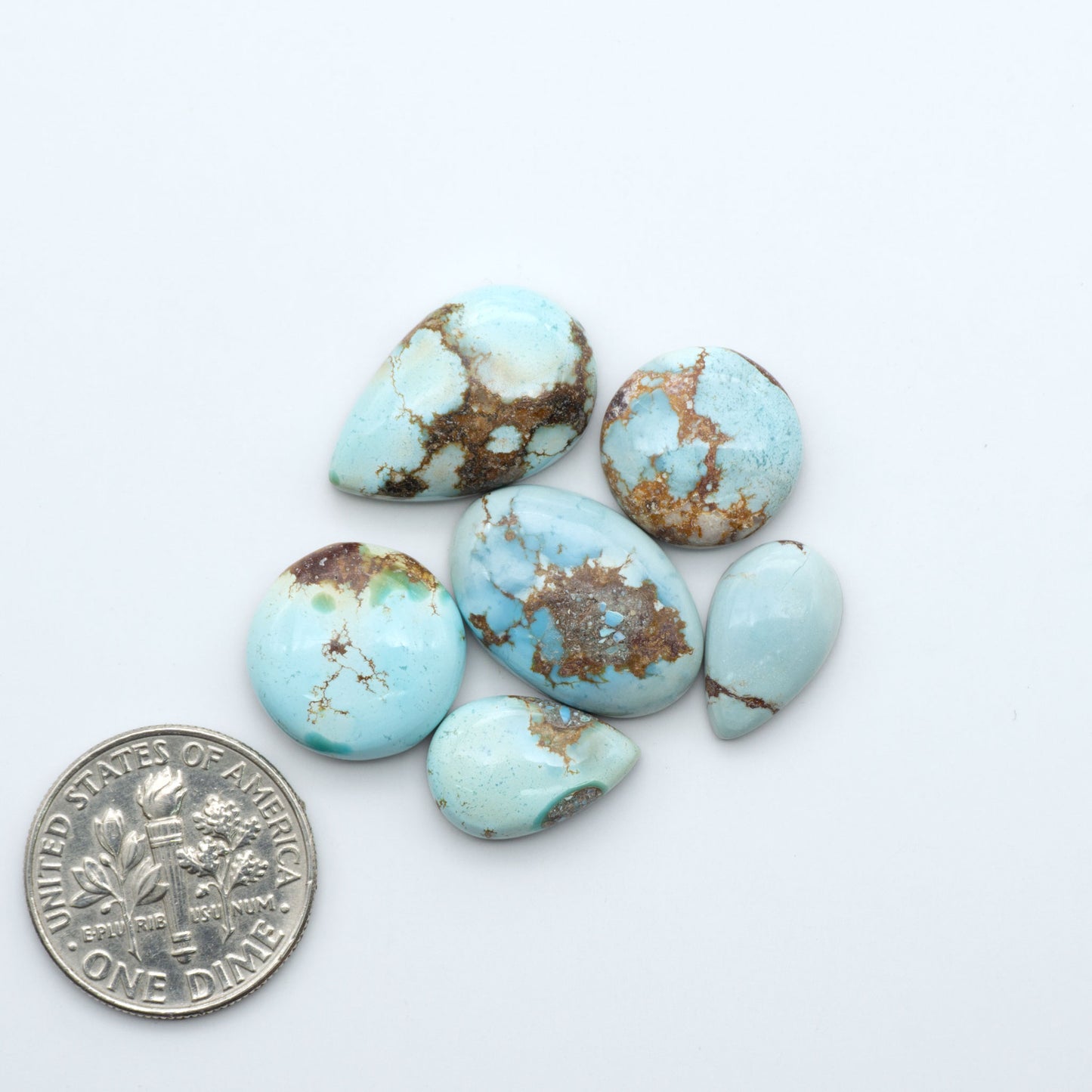 Golden Hills Turquoise cabochons, icy blue to lavender tones with chocolate matrix, polished stones on a white background with a US dime for scale