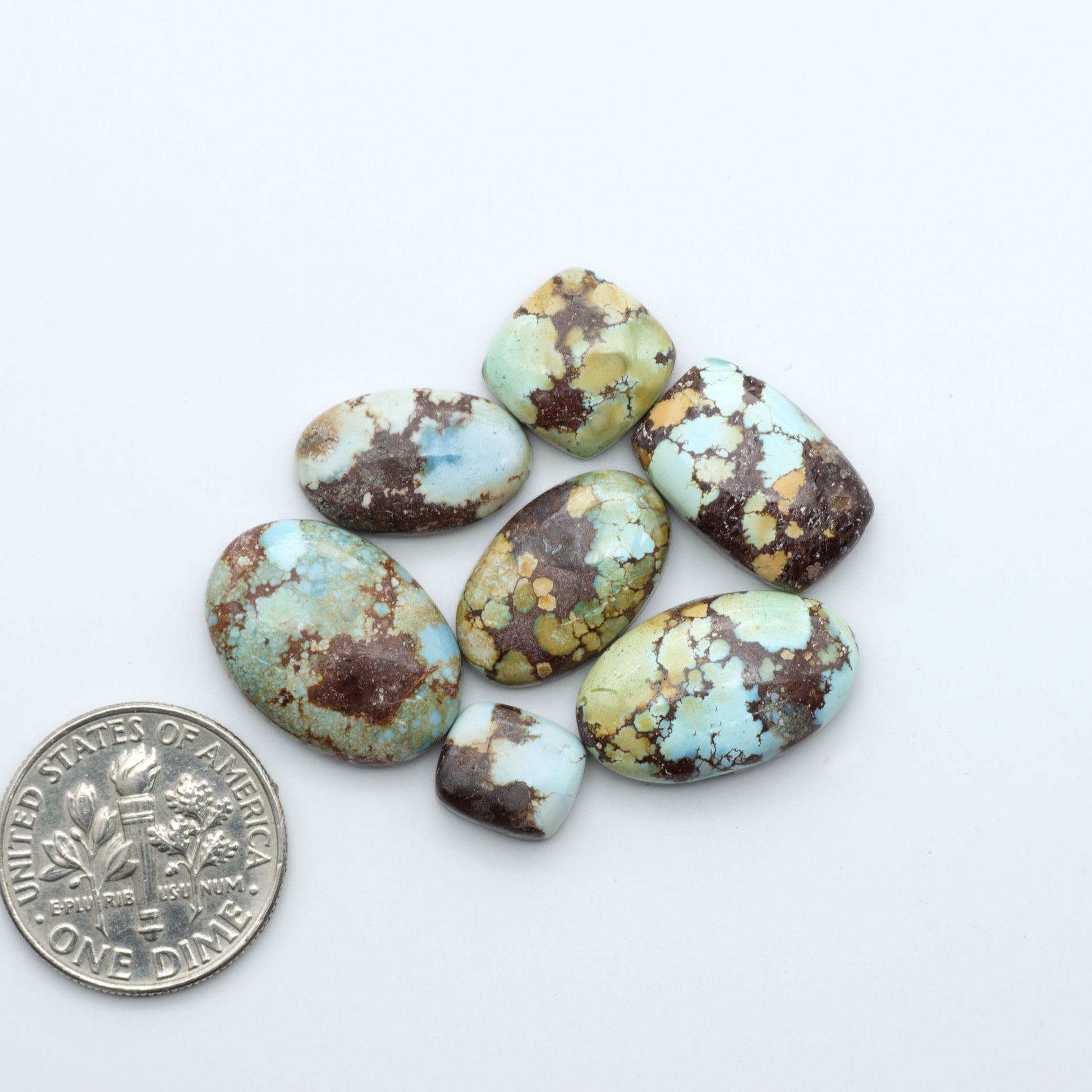 Golden Hills Turquoise cabochons, icy blue to lavender tones with chocolate matrix, polished stones on a white background with a US dime for scale