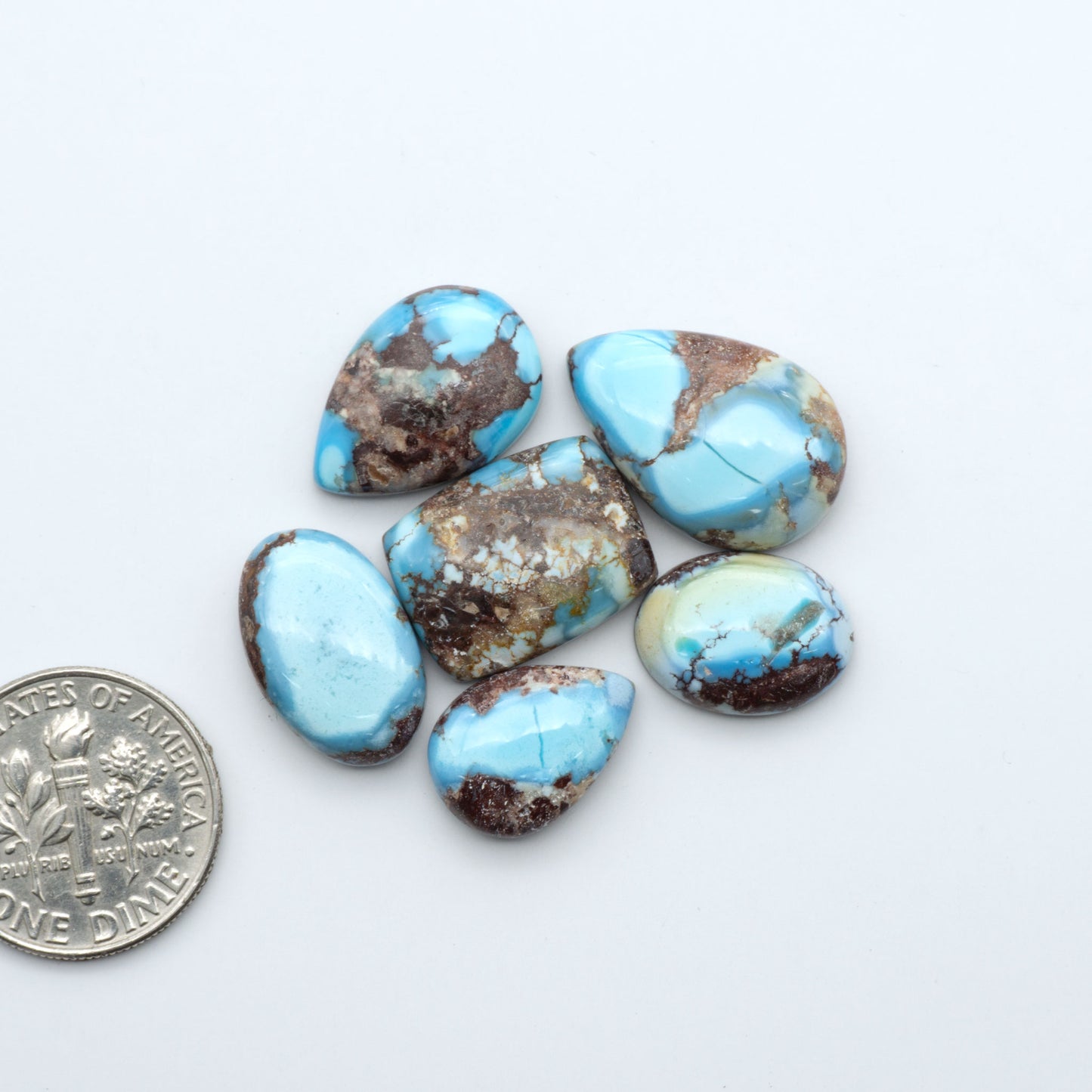 Golden Hills Turquoise cabochons, icy blue to lavender tones with chocolate matrix, polished stones on a white background with a US dime for scale