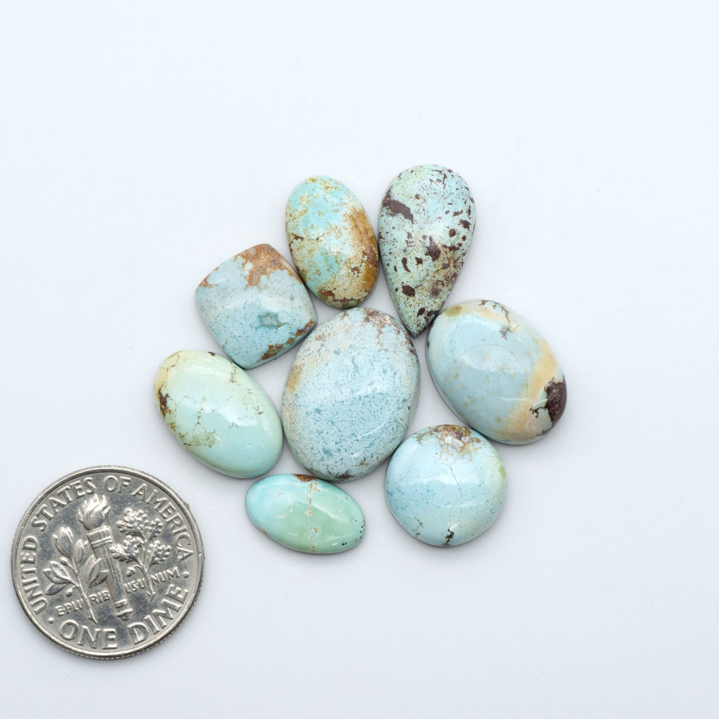 Golden Hills Turquoise cabochons, icy blue to lavender tones with chocolate matrix, polished stones on a white background with a US dime for scale