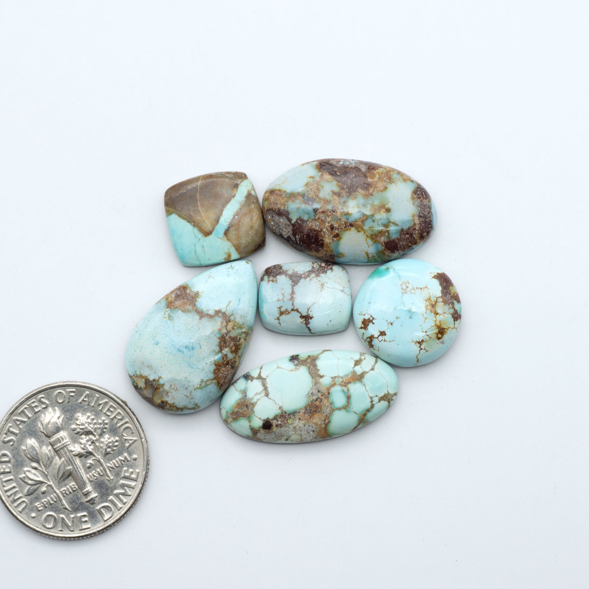 Golden Hills Turquoise cabochons, icy blue to lavender tones with chocolate matrix, polished stones on a white background with a US dime for scale