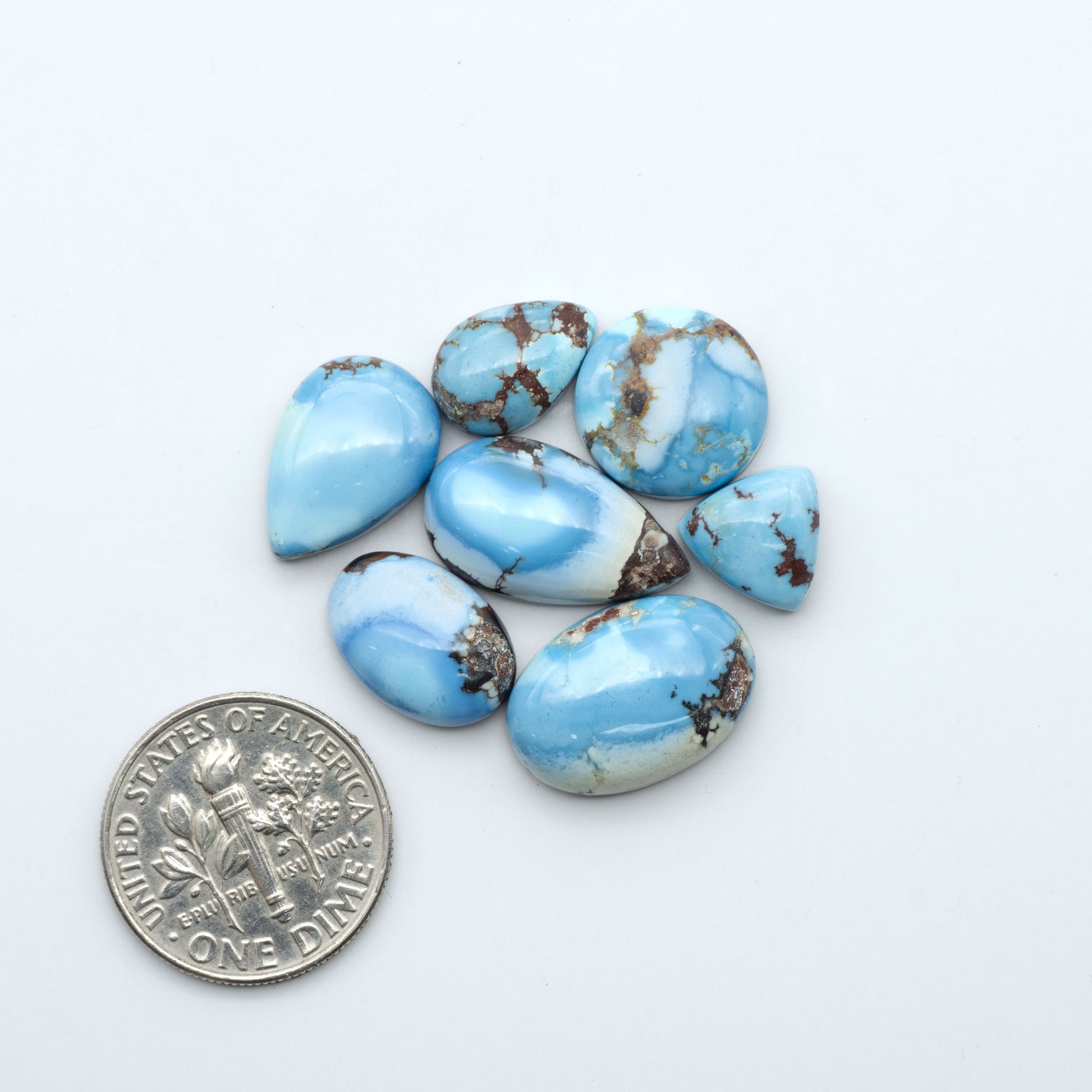 Golden Hills Turquoise cabochons, icy blue to lavender tones with chocolate matrix, polished stones on a white background with a US dime for scale