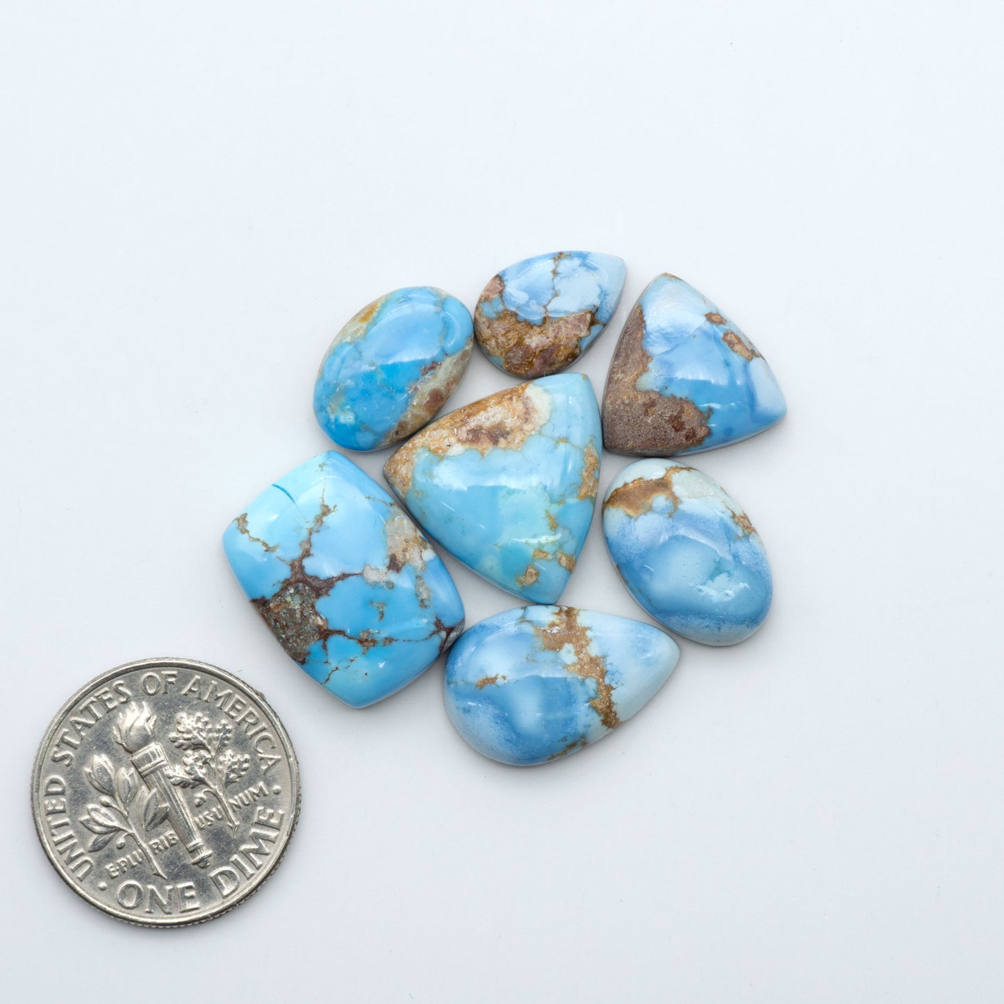 Golden Hills Turquoise cabochons, icy blue to lavender tones with chocolate matrix, polished stones on a white background with a US dime for scale