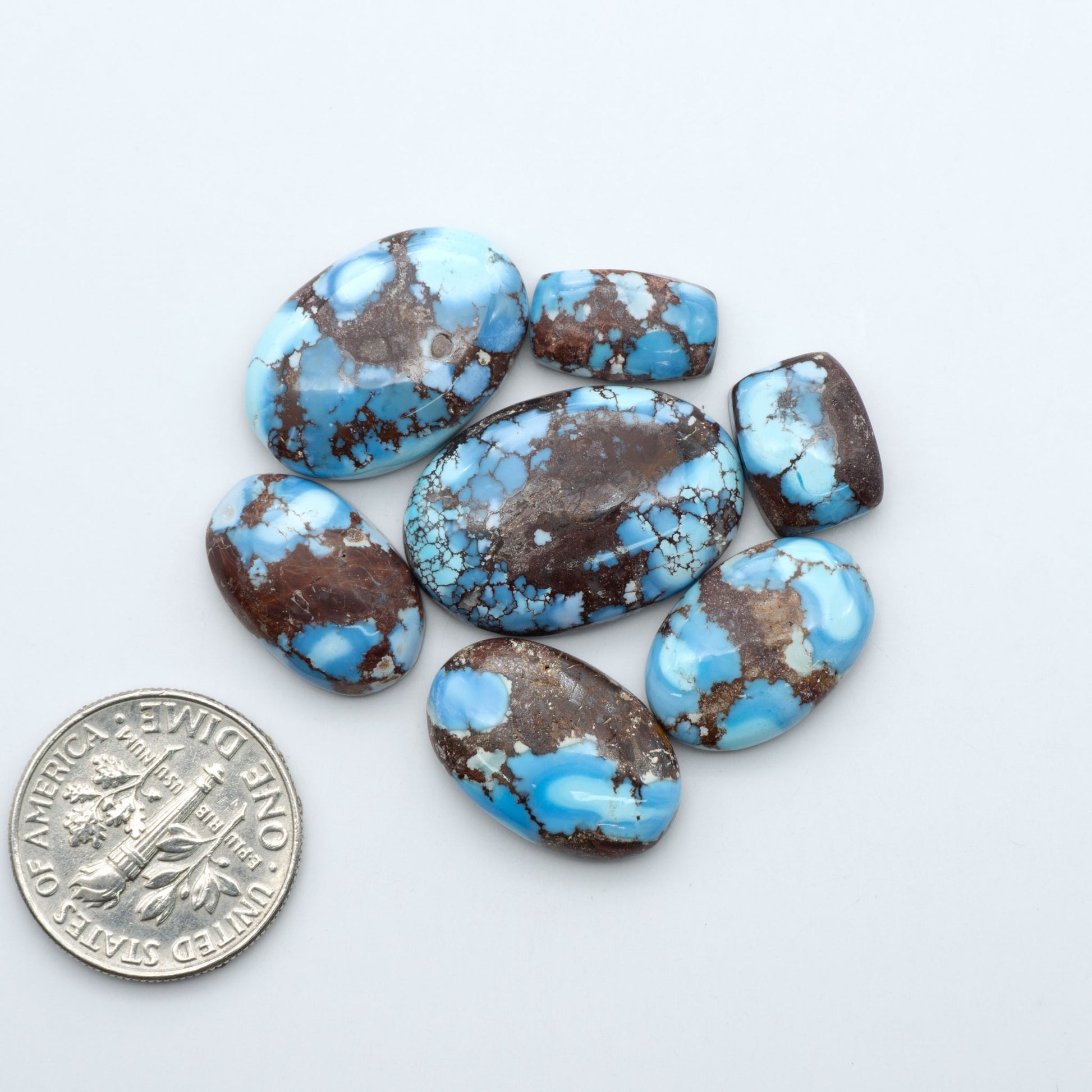 Golden Hills Turquoise cabochons, icy blue to lavender tones with chocolate matrix, polished stones on a white background with a US dime for scale