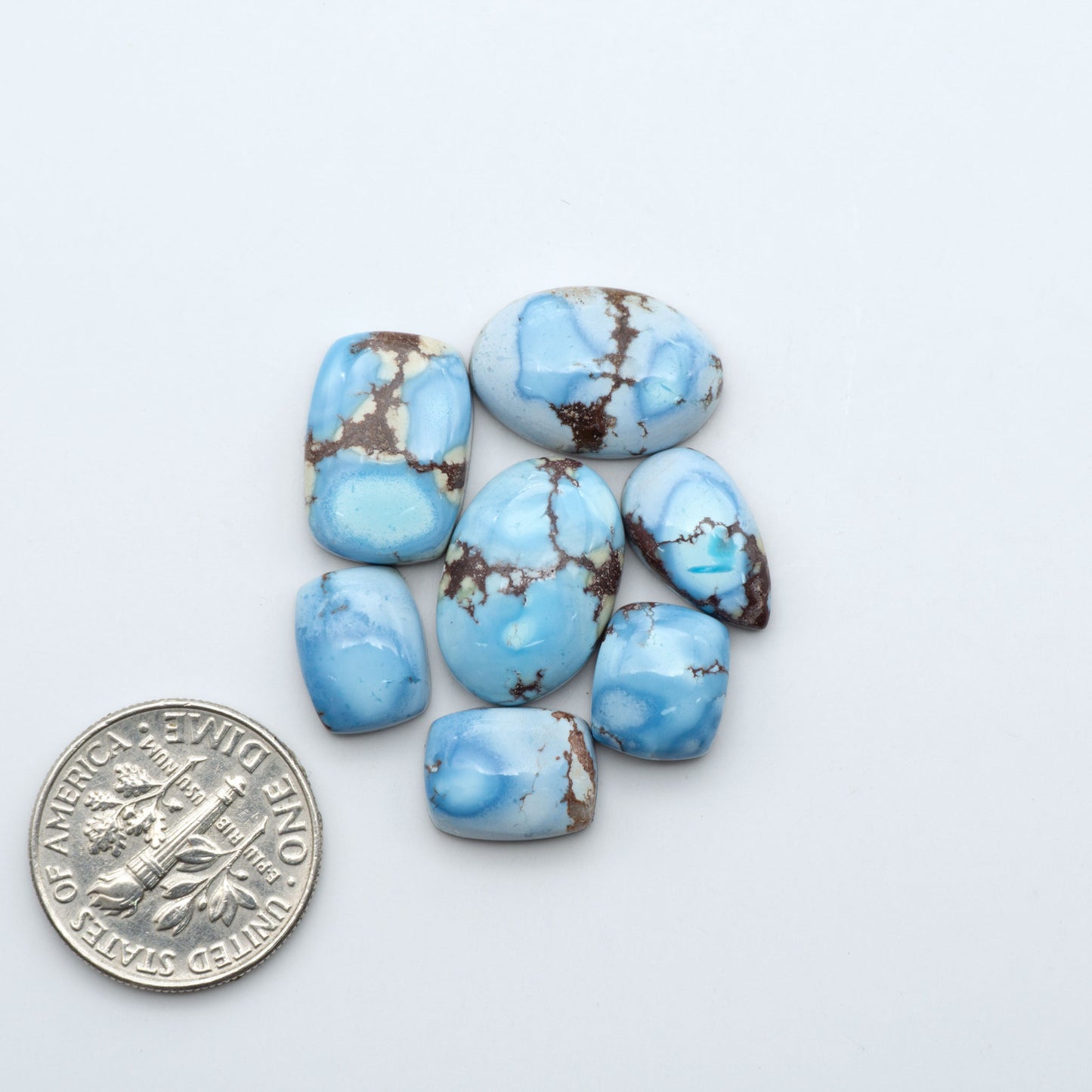 Golden Hills Turquoise cabochons, icy blue to lavender tones with chocolate matrix, polished stones on a white background with a US dime for scale