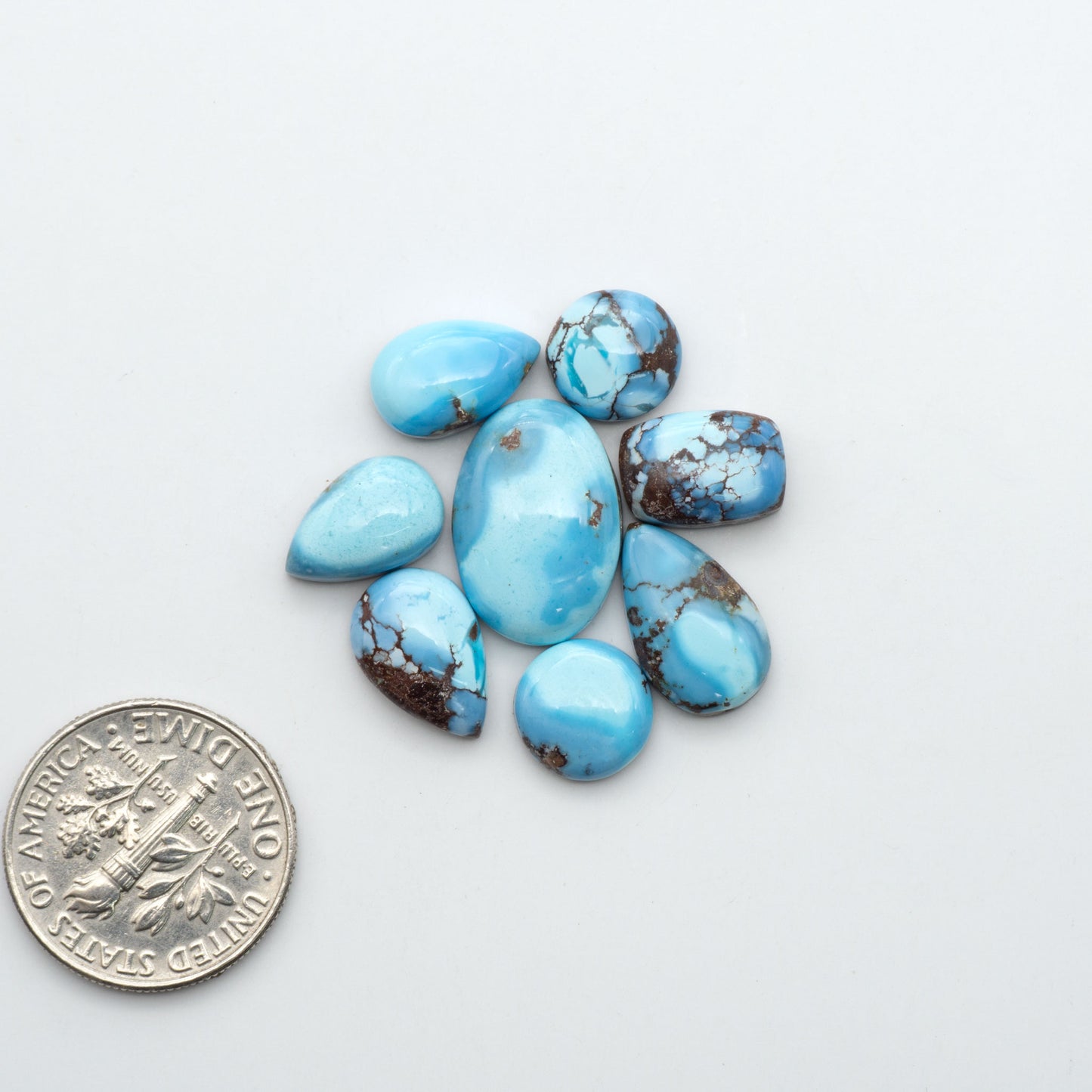 Golden Hills Turquoise cabochons, icy blue to lavender tones with chocolate matrix, polished stones on a white background with a US dime for scale
